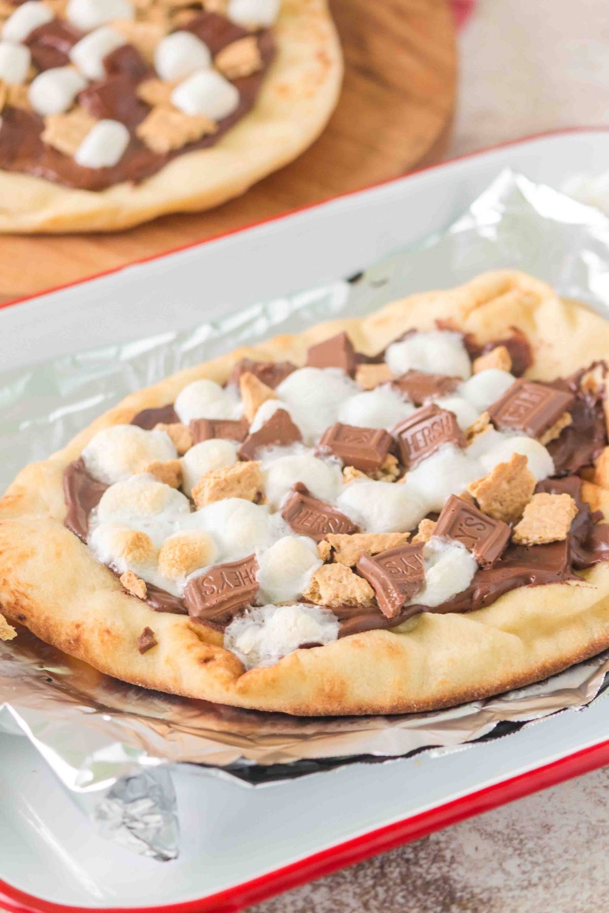 Flatbread topped with melted chocolate, marshmallows, graham cracker pieces, and chocolate chunks on foil.