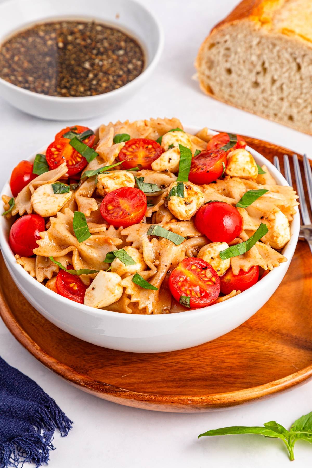 A bowl of bow-tie pasta salad with cherry tomatoes, mozzarella, and basil, served on a wooden plate.