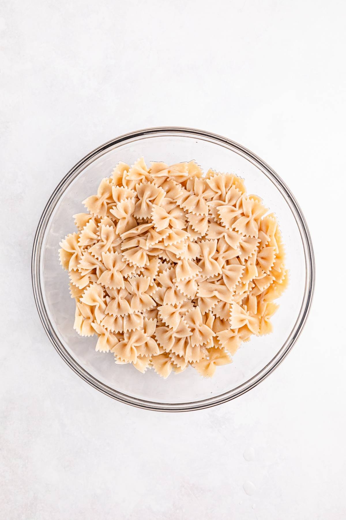 A glass bowl filled with cooked farfalle pasta on a white surface.