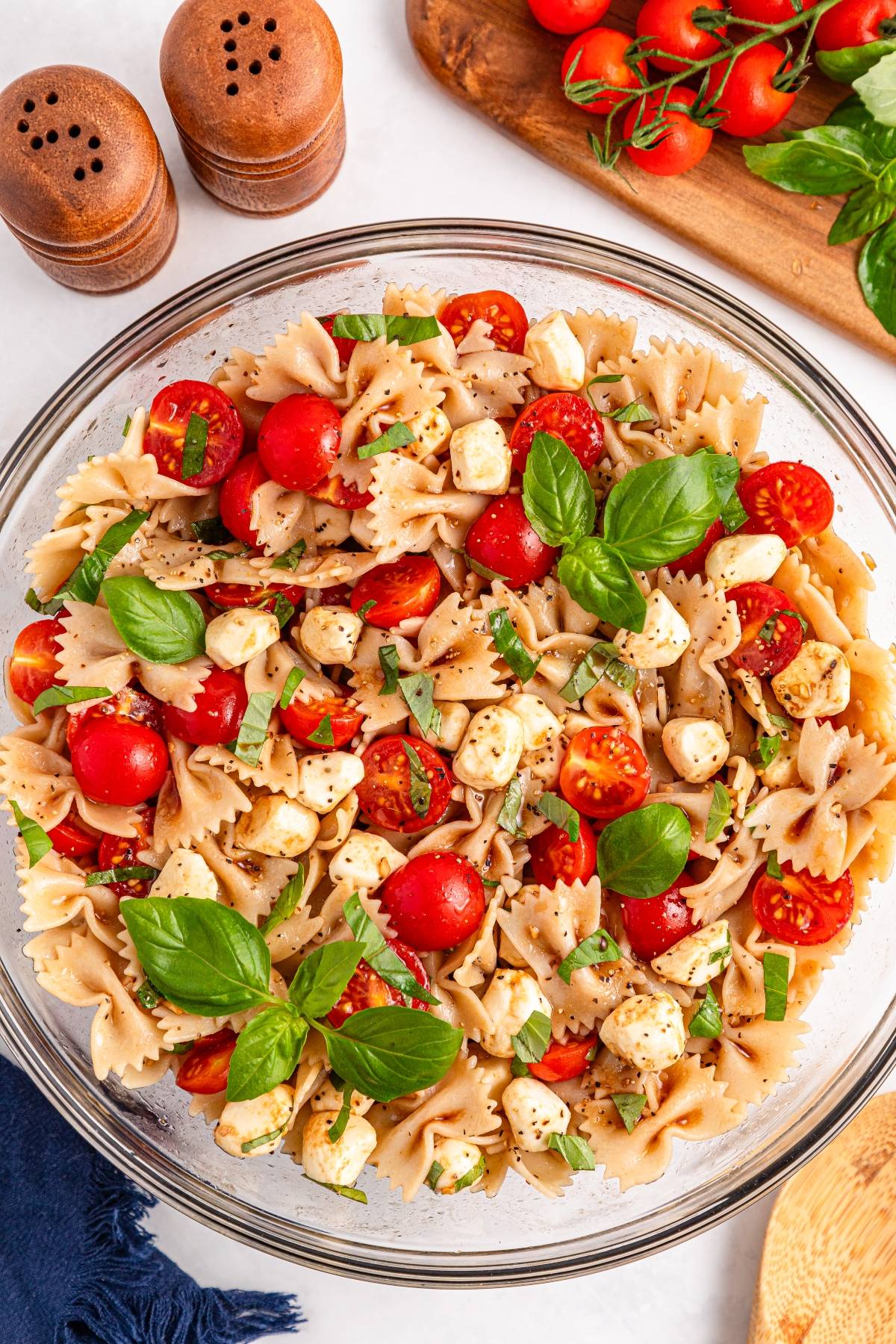 Bowtie pasta salad with cherry tomatoes, mozzarella balls, fresh basil, and black pepper in a glass bowl.