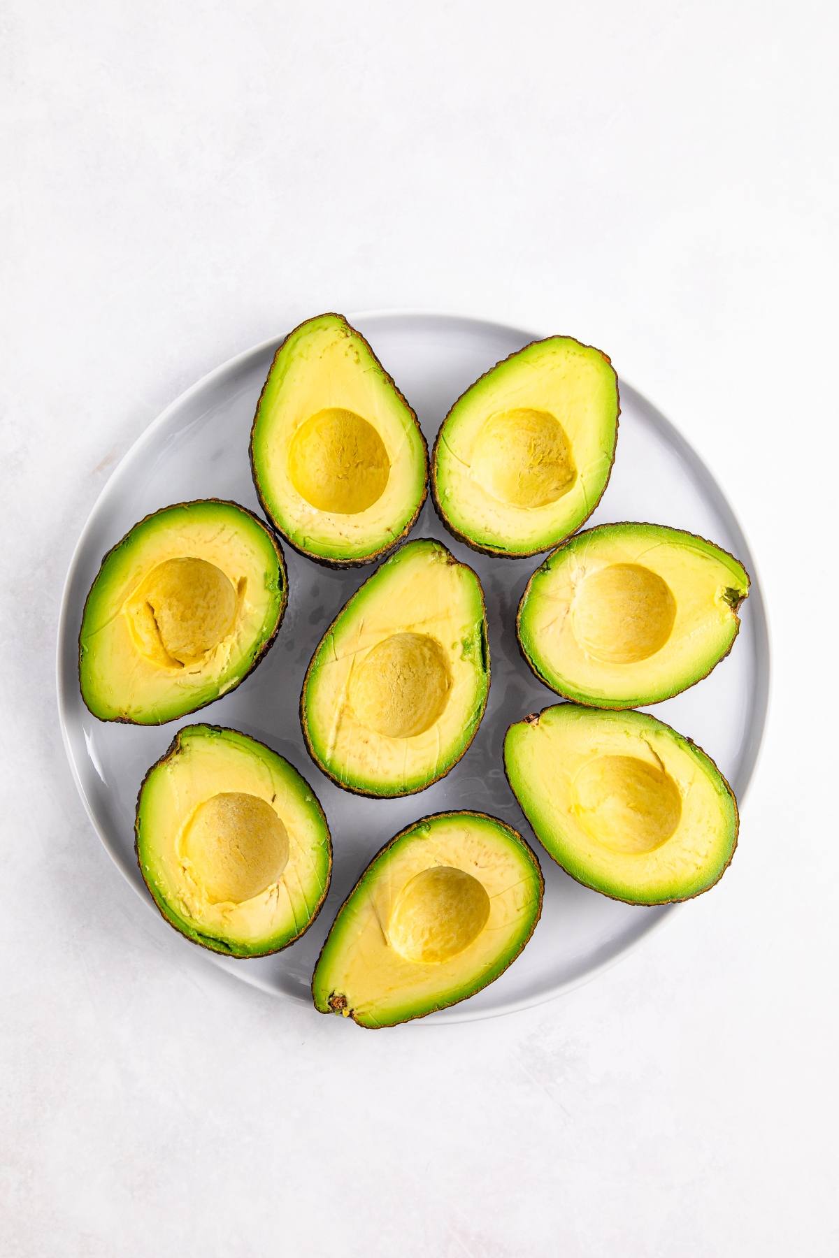 A gray plate with six halved avocados, arranged neatly on a white background.