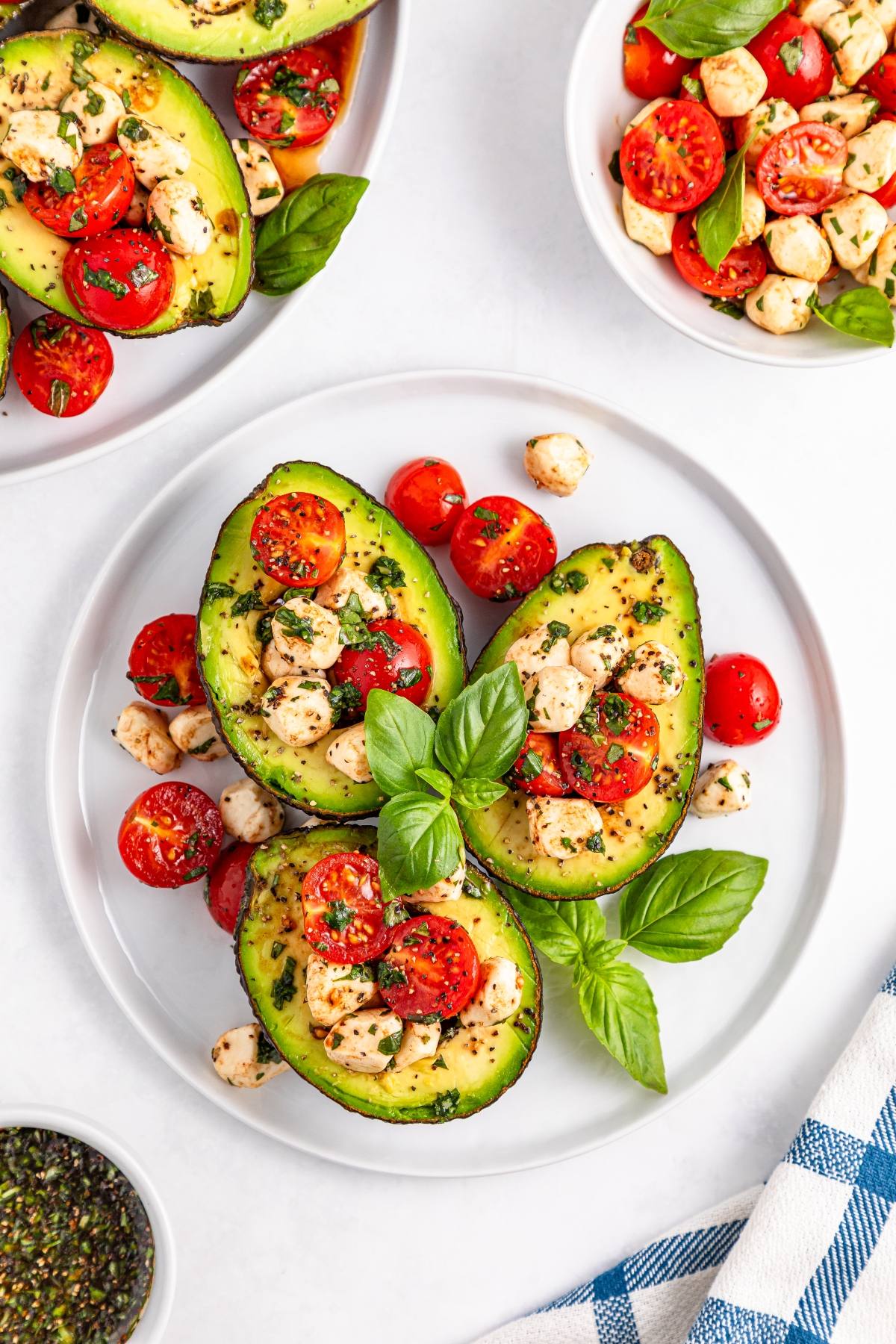 Halved avocados filled with tomato, mozzarella, herbs, and basil leaves on a white plate.