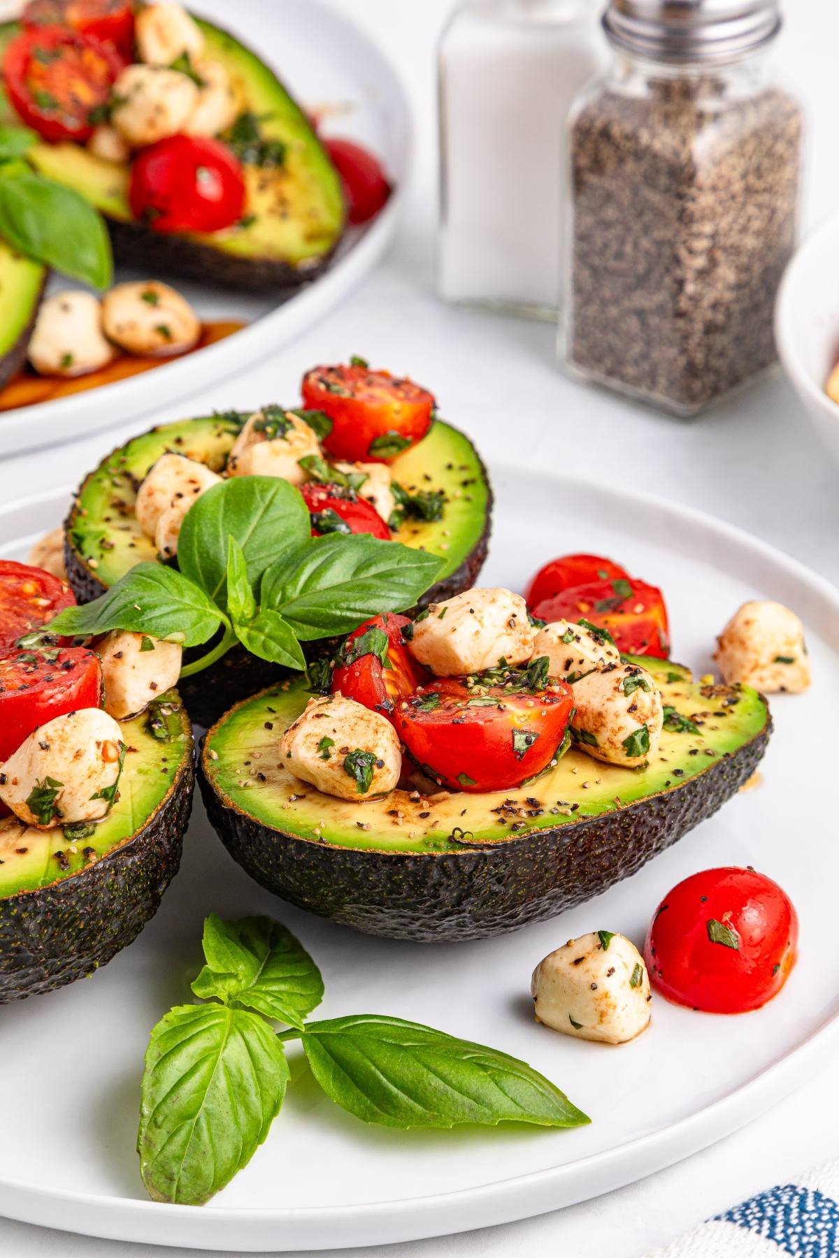 Halved avocados filled with mozzarella, cherry tomatoes, and basil on a white plate.
