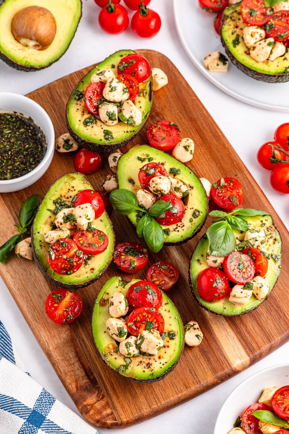 Avocado halves filled with cherry tomatoes, mozzarella, and herbs on a wooden board, garnished with basil.