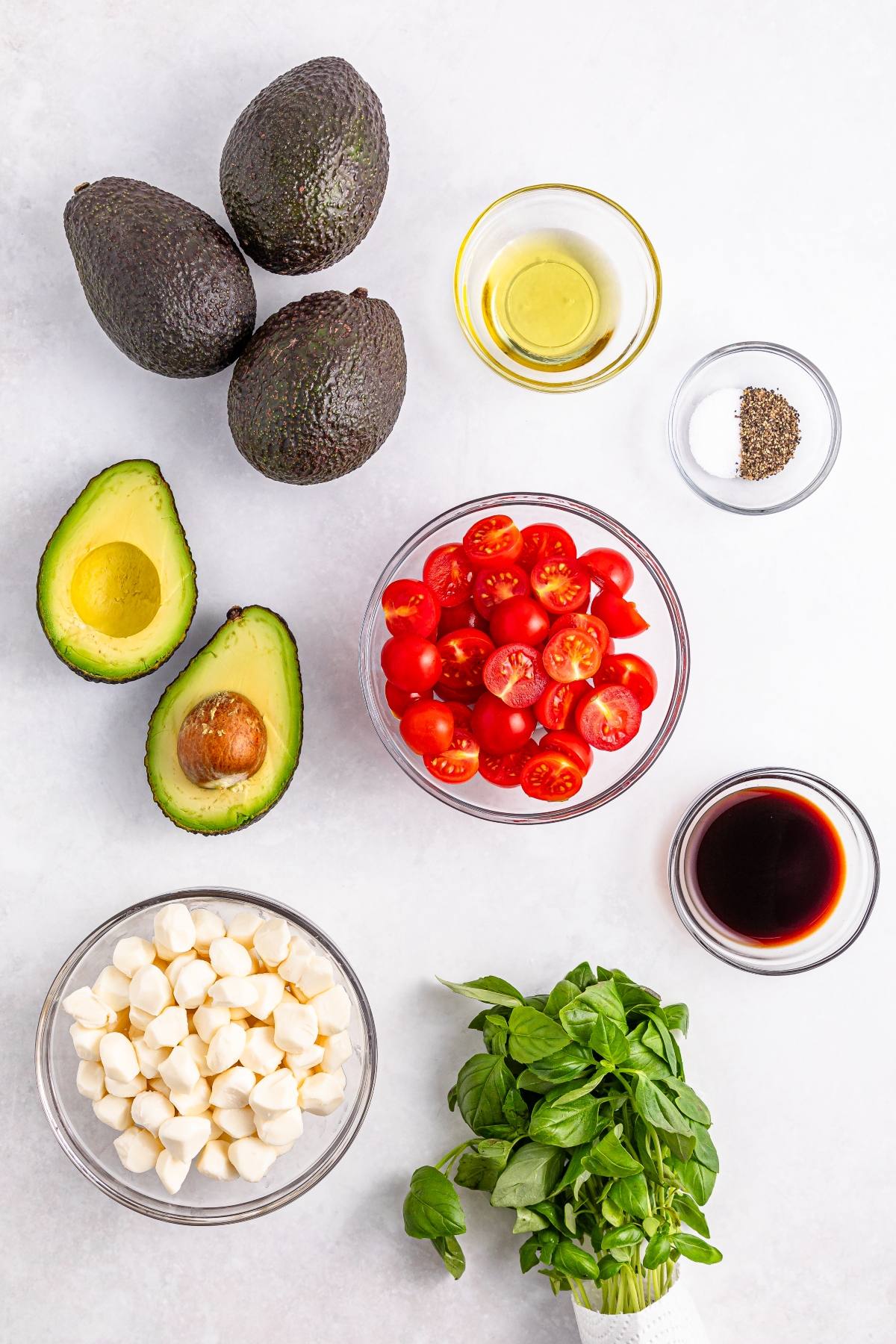 Whole and halved avocados, cherry tomatoes, mozzarella balls, basil, olive oil, balsamic, salt, and pepper.