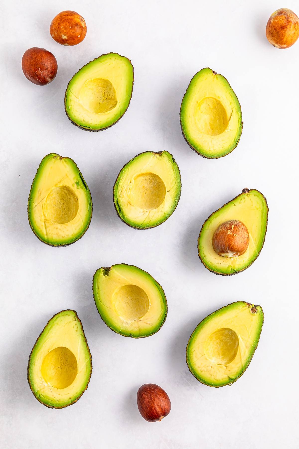 Halved avocados and avocado pits arranged on a white background.
