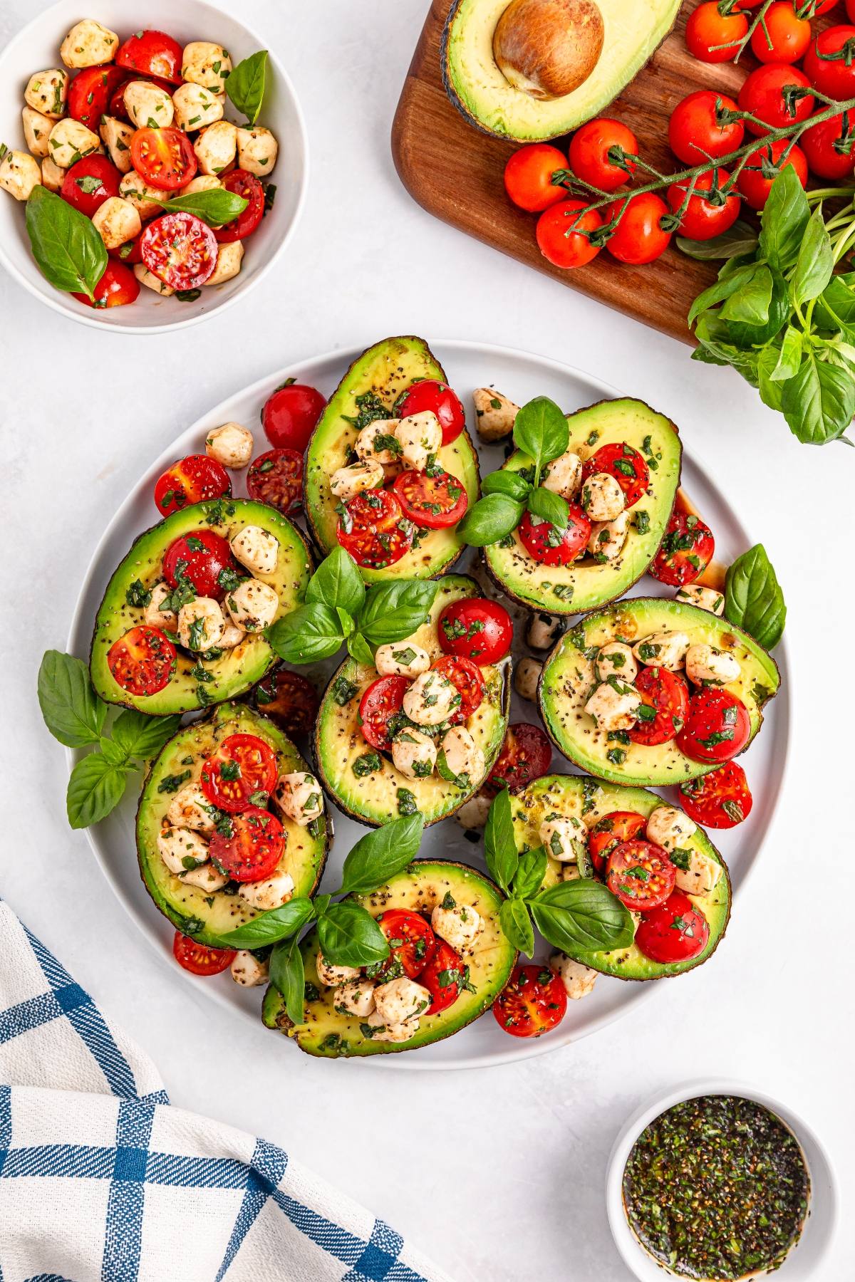 Halved avocados filled with mozzarella, cherry tomatoes, and herbs, garnished with fresh basil on a plate.