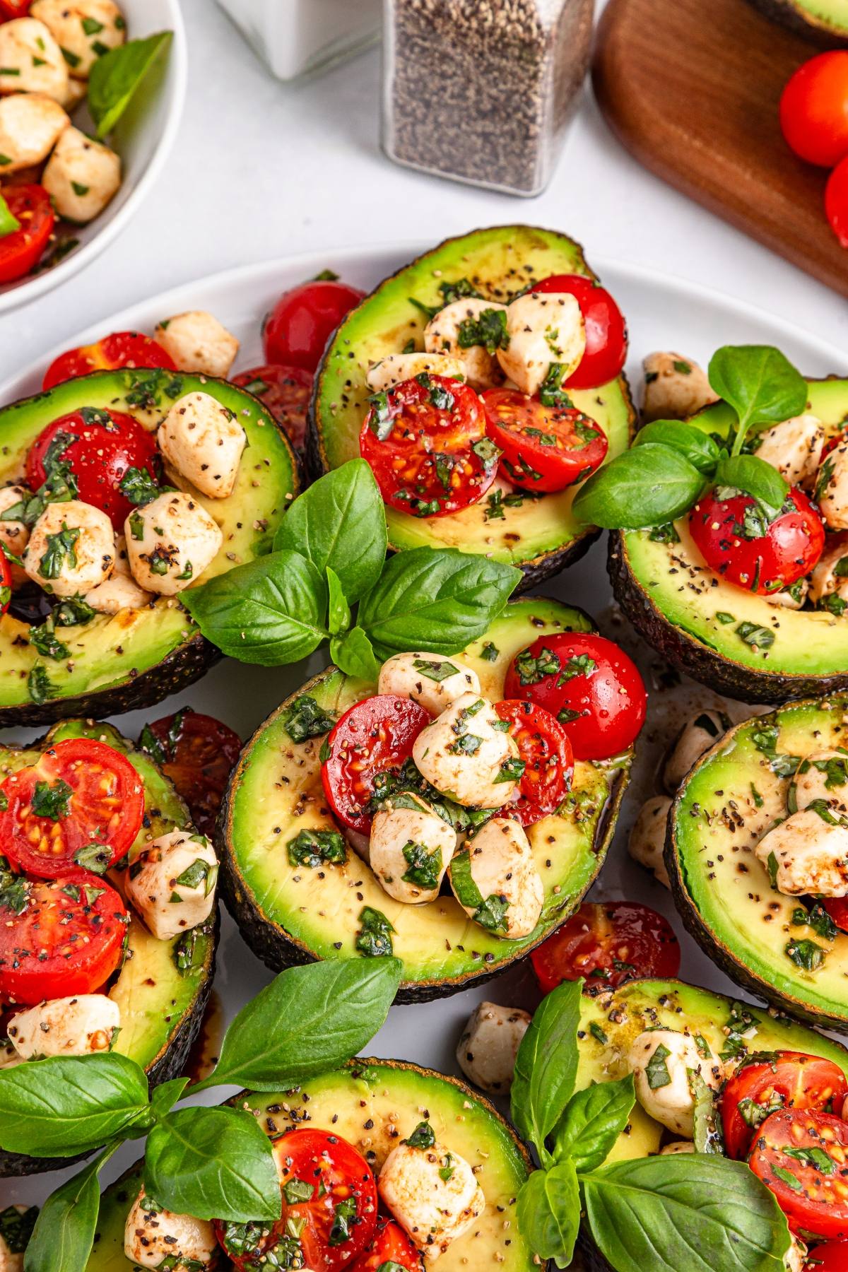 Halved avocados filled with cherry tomatoes, mozzarella balls, herbs, and fresh basil leaves.