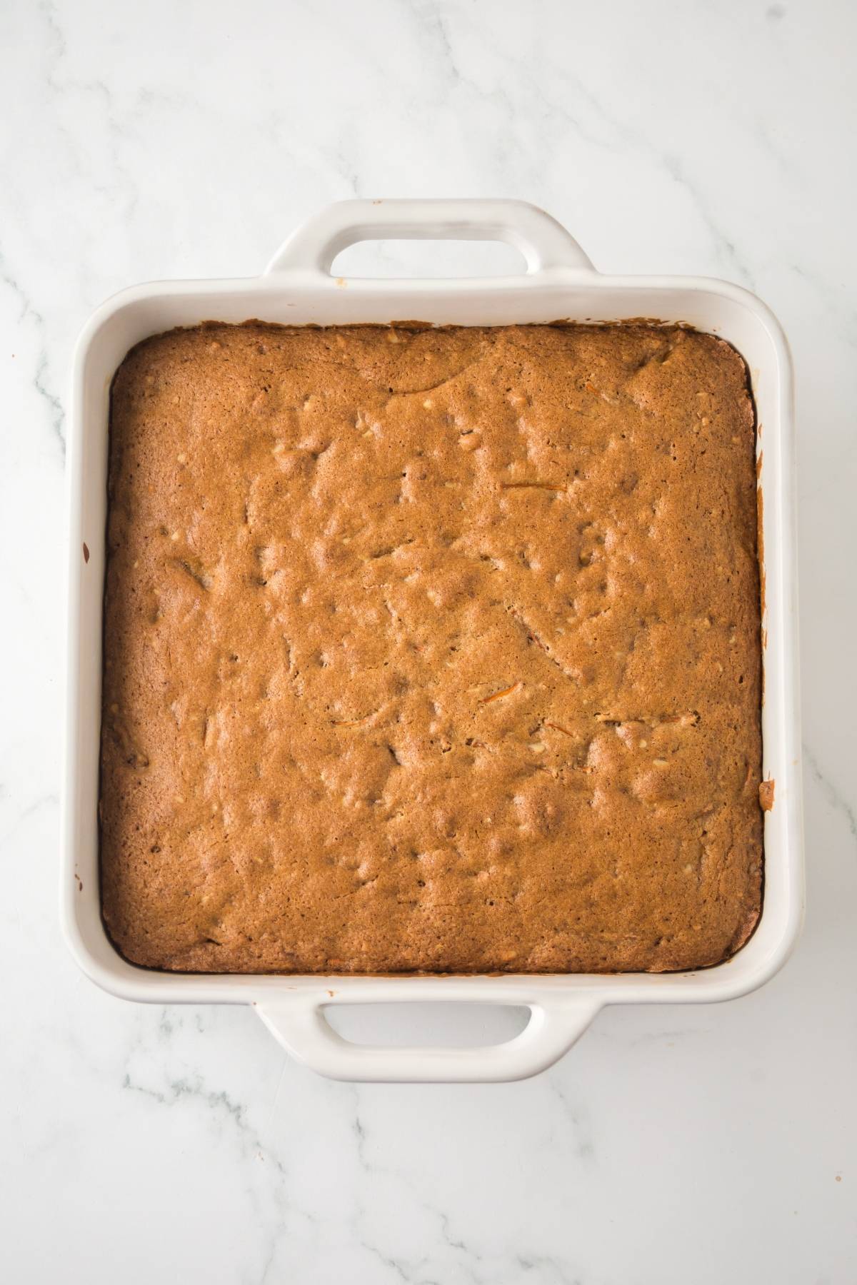 Golden brown cake baked in a white square dish on a marble countertop, viewed from above.