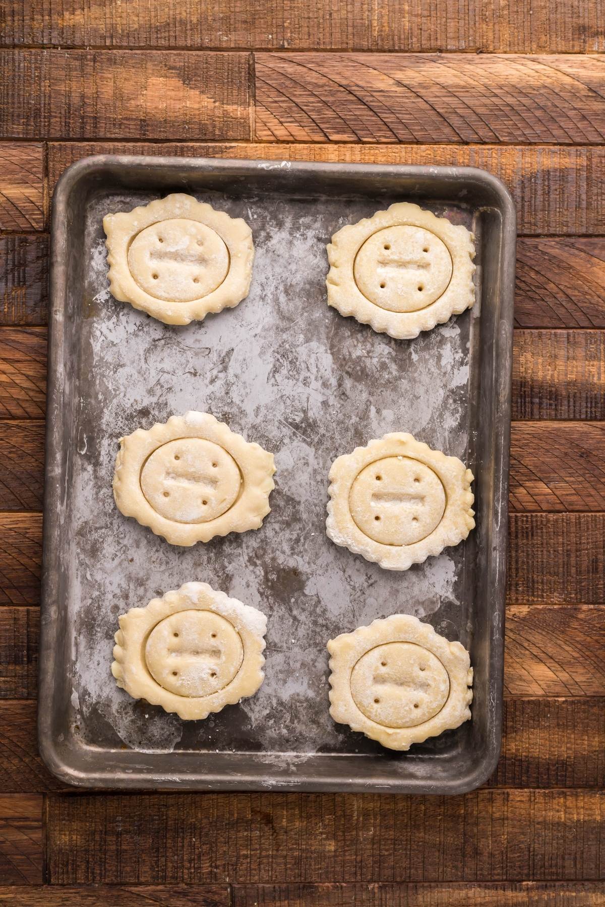 Six unbaked Cherry Cream Cheese Puff Pastries rest on a floured baking tray atop a wooden surface, ready to be baked into delicious treats.