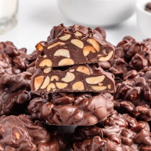 A plate of Crockpot Candy chocolate nut clusters, with one cut in half to reveal the delicious nuts inside.