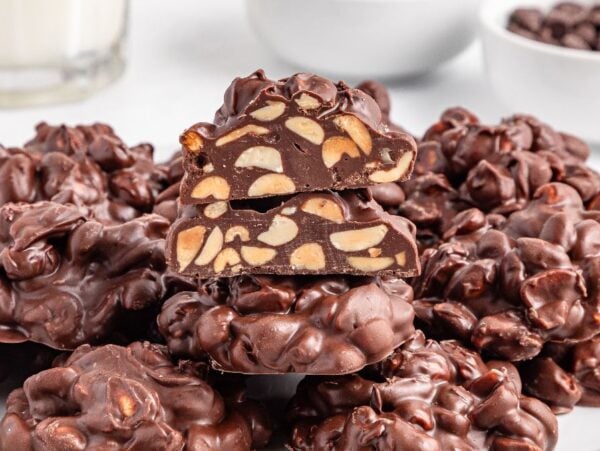 A plate of Crockpot Candy chocolate nut clusters, with one cut in half to reveal the delicious nuts inside.