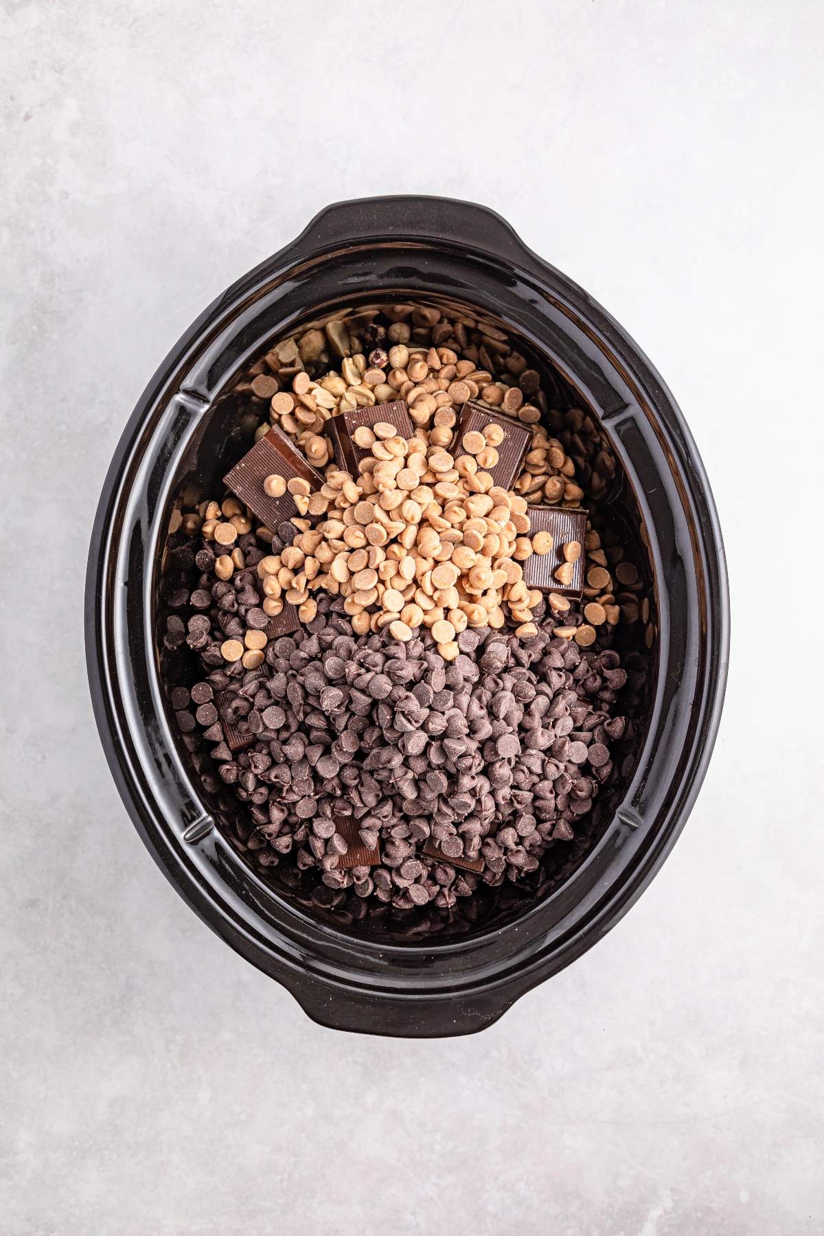 Chocolate chips, peanut butter chips, and chocolate bars in a slow cooker, viewed from above.