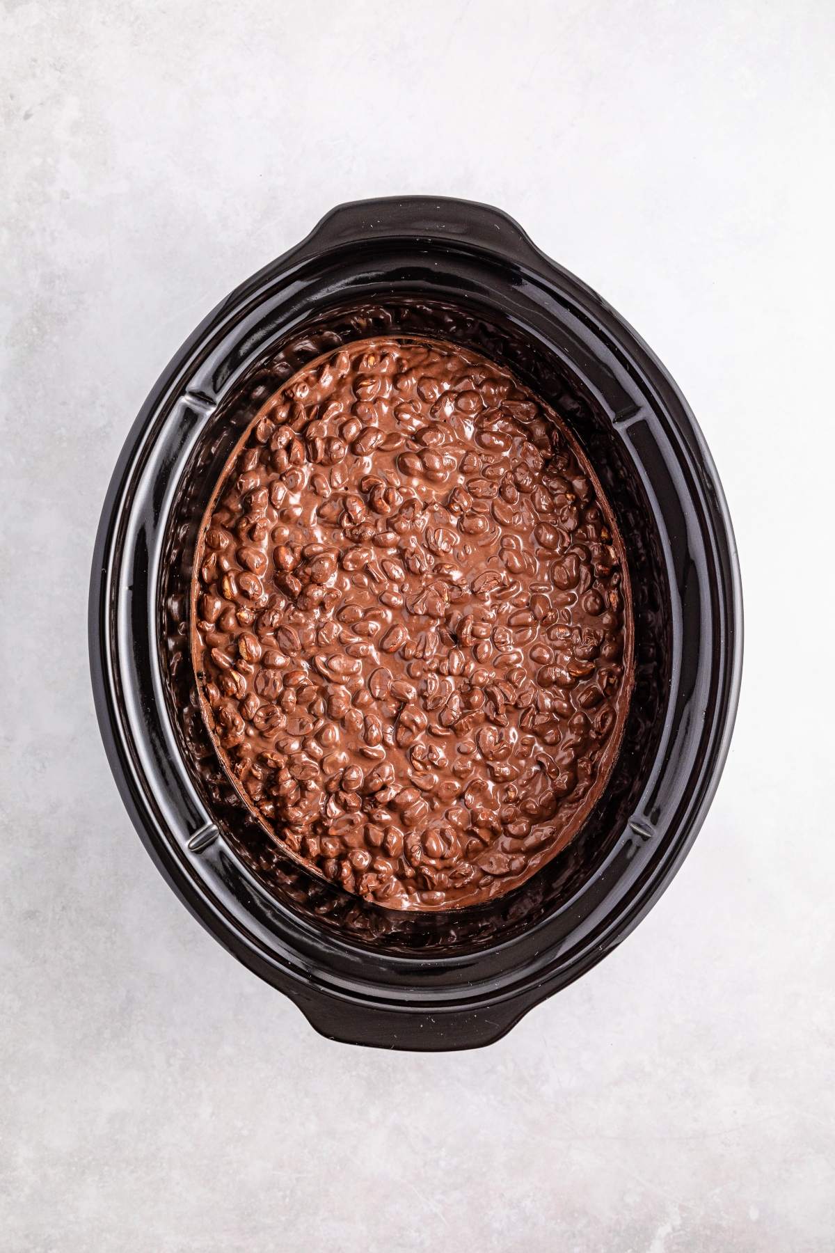Chocolate cake batter in a black slow cooker, ready to be baked, on a light gray background.