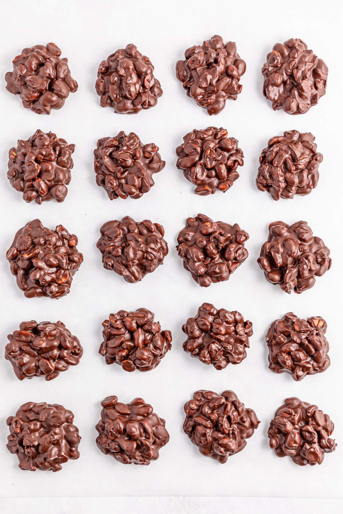 Twenty clusters of chocolate nut candies arranged neatly in a grid pattern on a white surface.