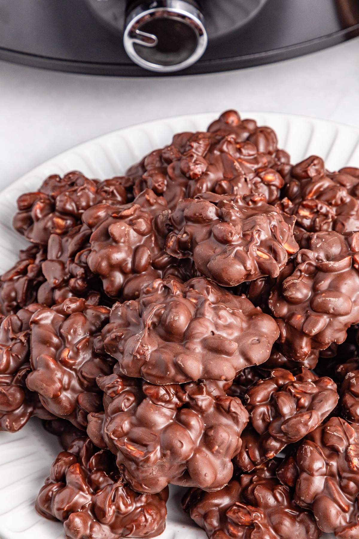 A plate piled with clusters of chocolate-covered nuts in front of a slow cooker.