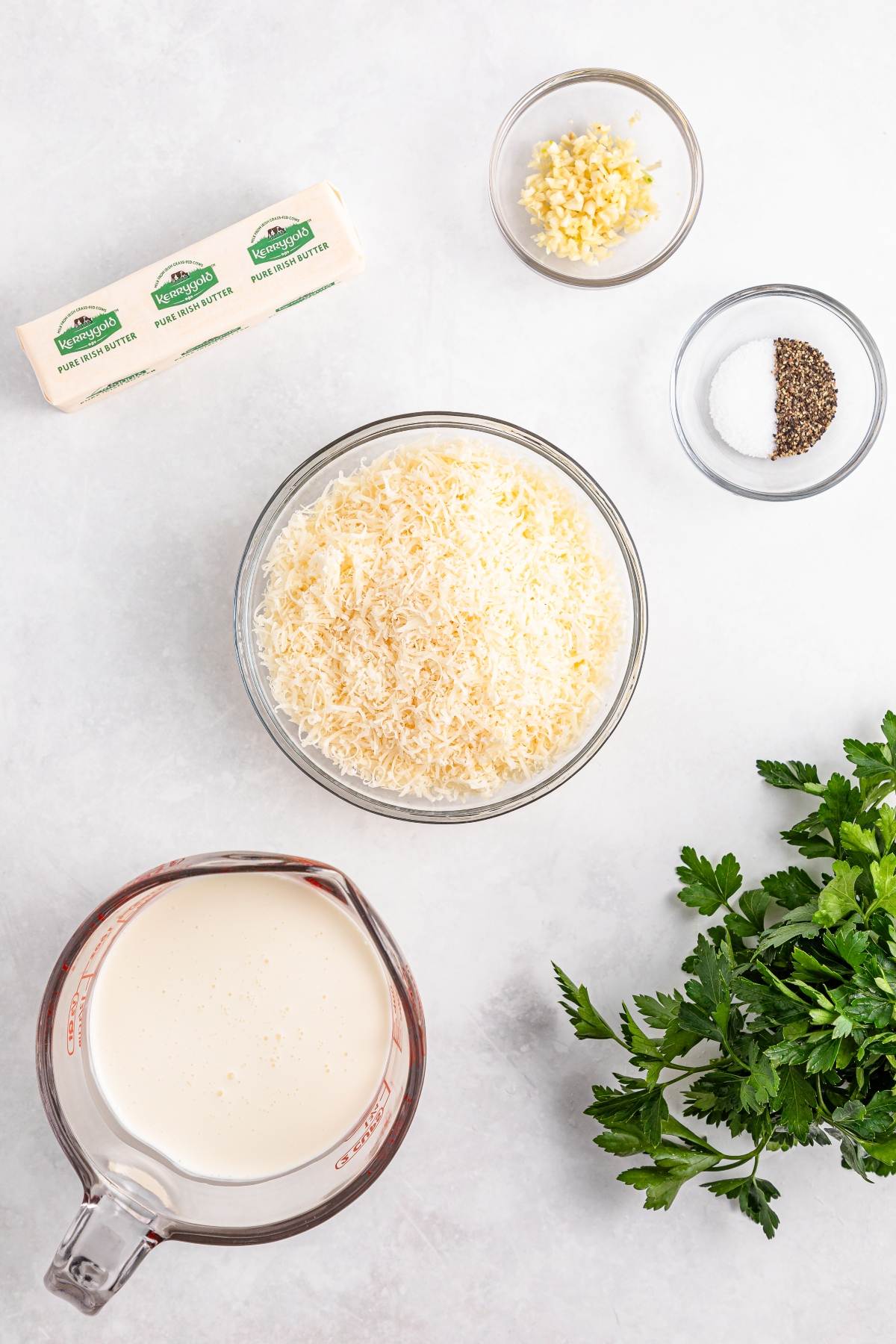 Ingredients for Alfredo sauce: butter, minced garlic, salt and pepper, grated cheese, cream, and fresh parsley.