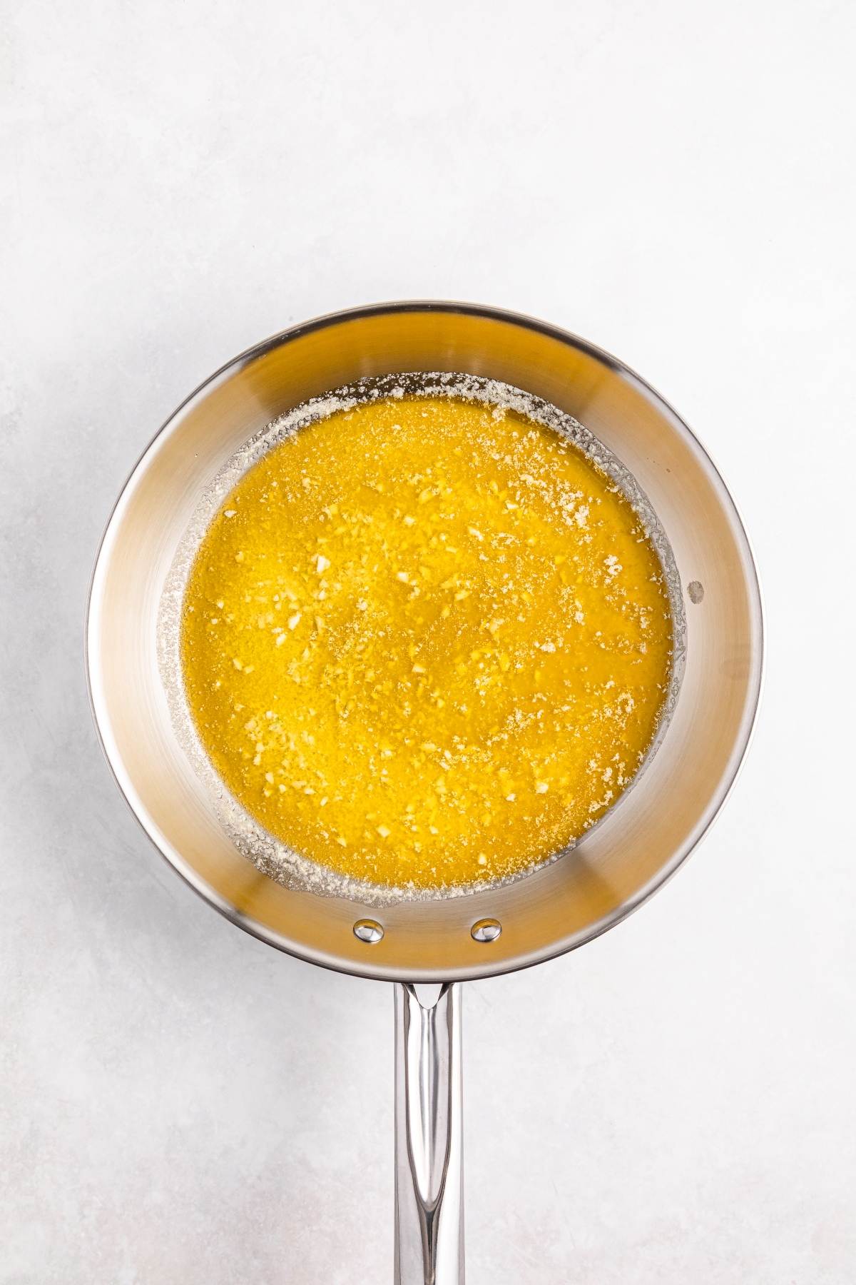 Butter melting and bubbling in a stainless steel saucepan on a light-colored surface.