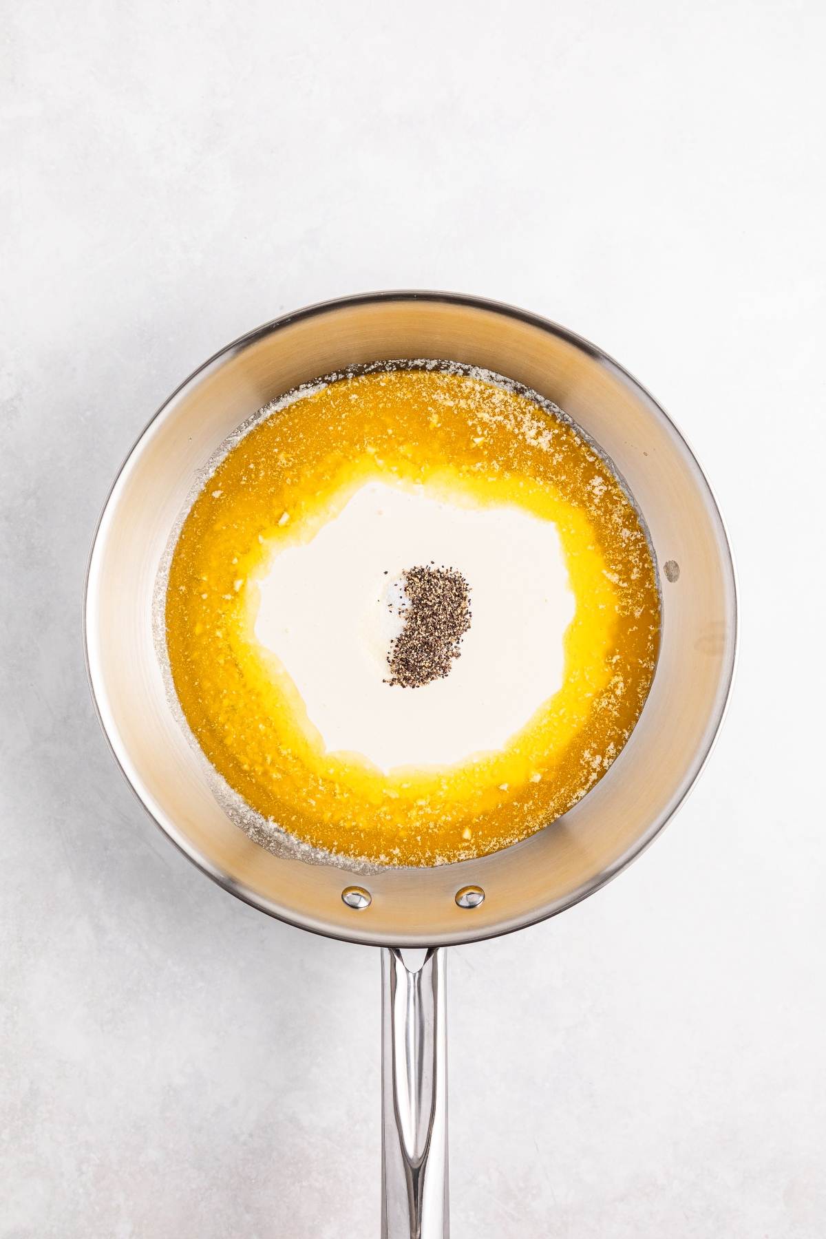 A saucepan with melted butter, cream, and black pepper on a light surface.