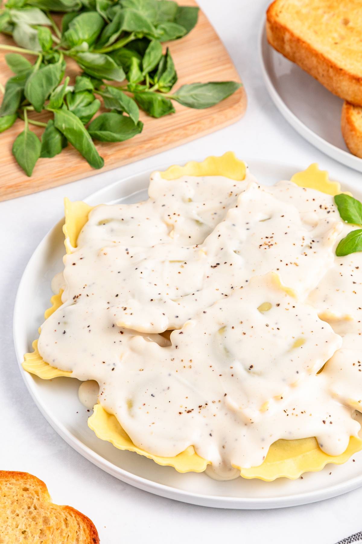 Ravioli topped with creamy white sauce and black pepper, served with toast and fresh greens on the side.