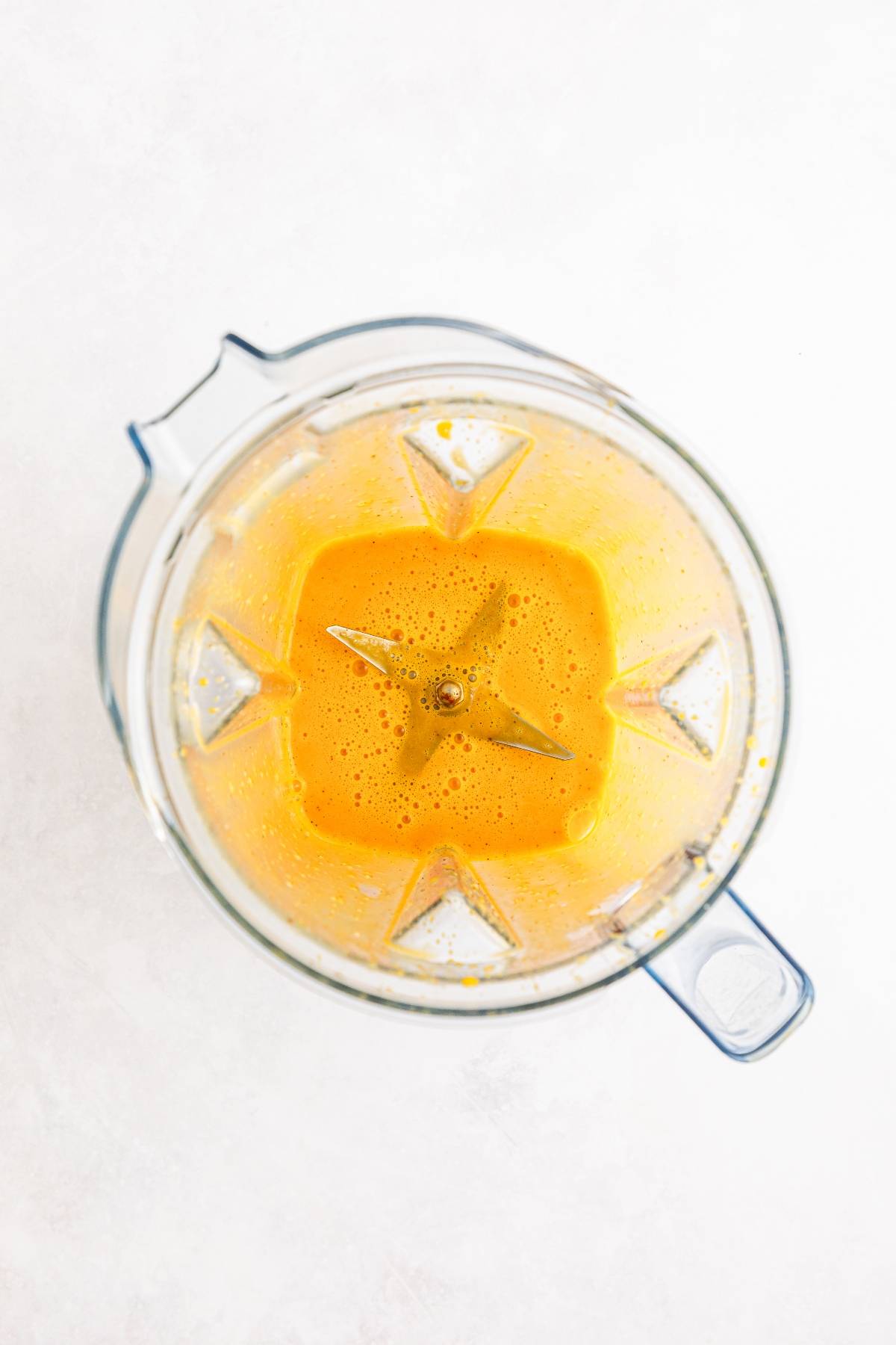 Top view of a blender containing a smooth, bright orange liquid on a white background.