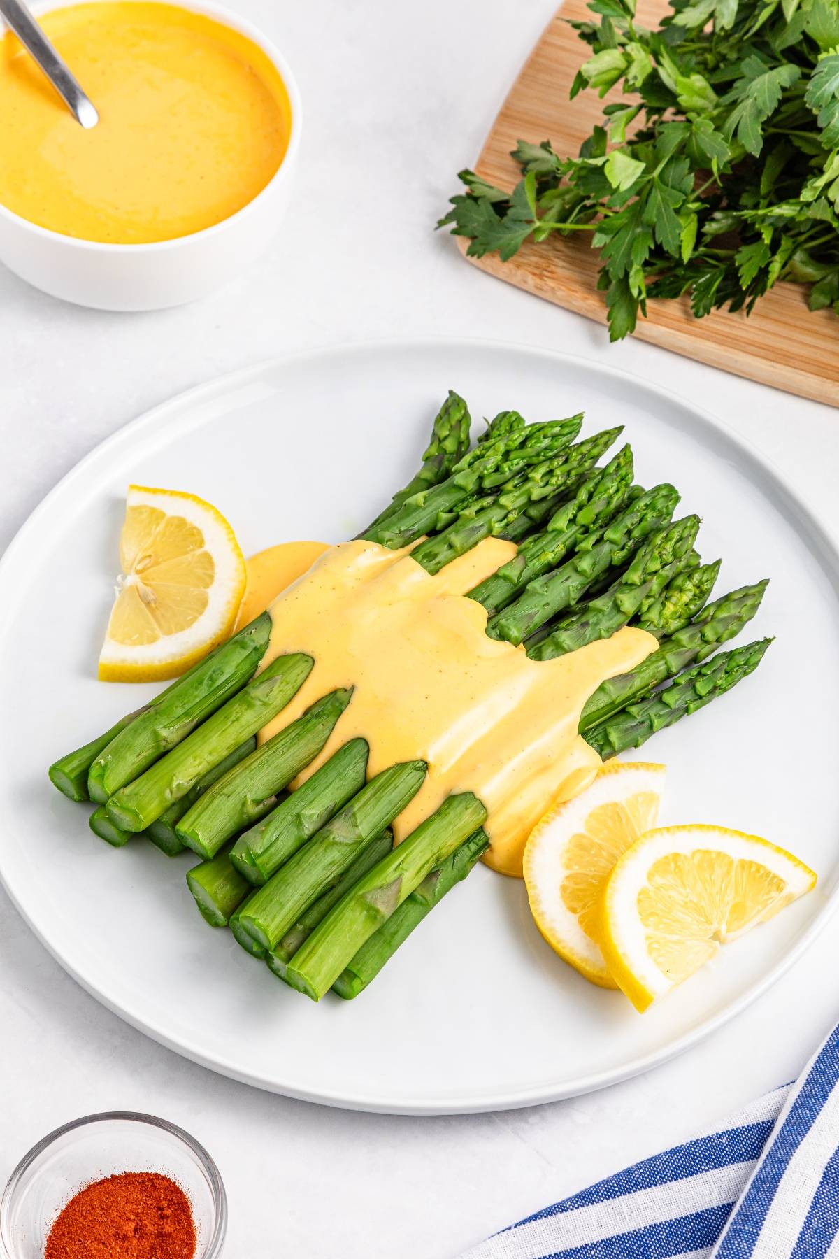 Steamed asparagus topped with hollandaise sauce, garnished with lemon slices on a white plate.