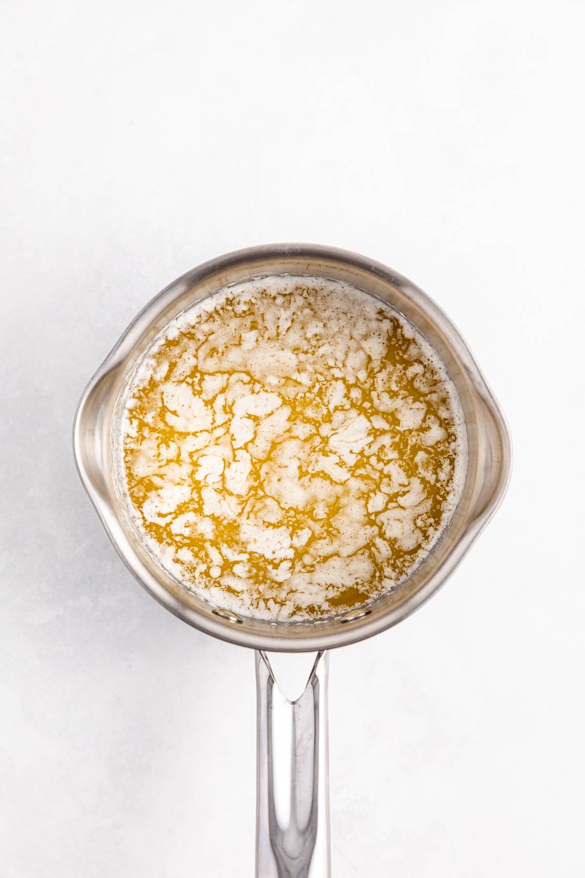 A saucepan filled with melted butter showing white milk solids floating on the surface.