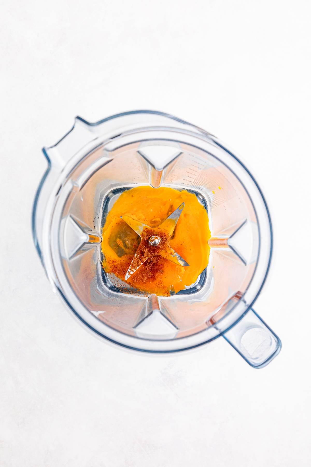 Overhead view of orange liquid and spices in a blender, ready to be mixed.