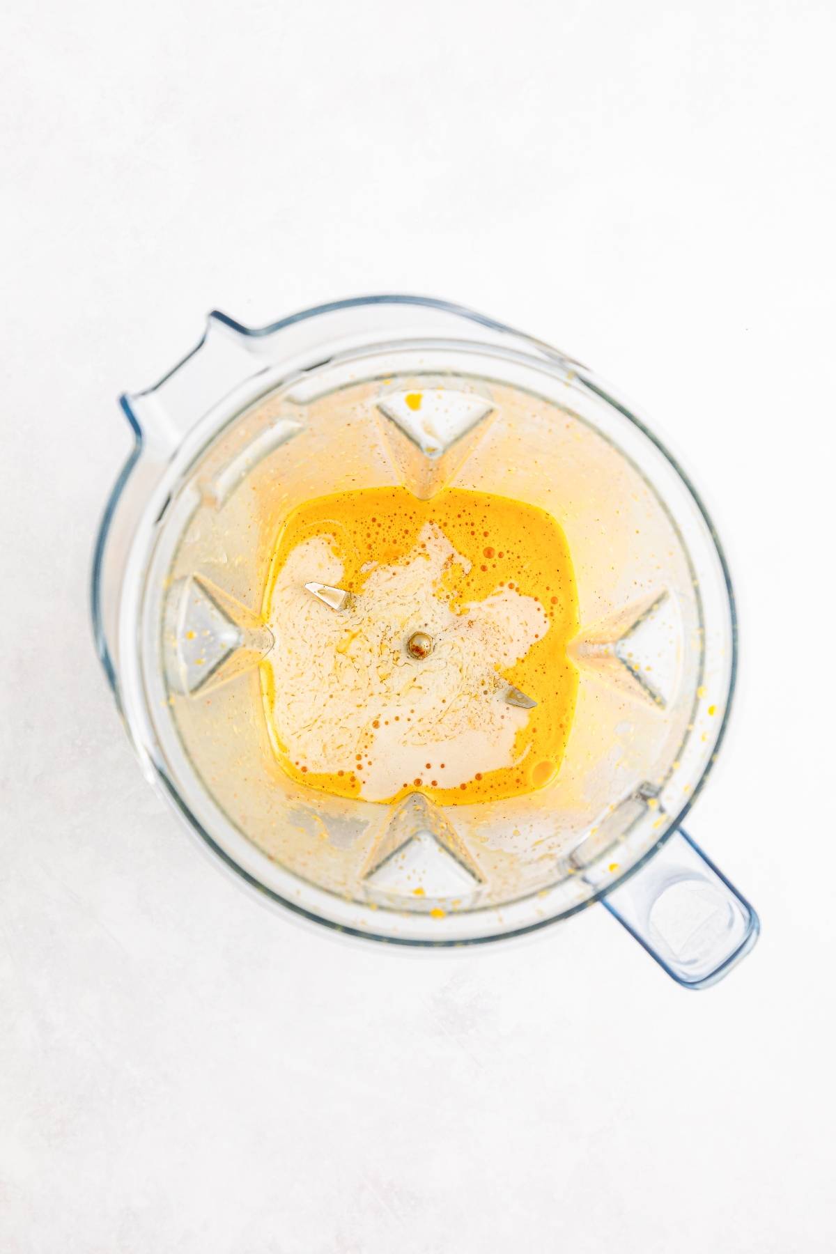 Overhead view of a blender containing a bright yellow liquid mixture on a white surface.