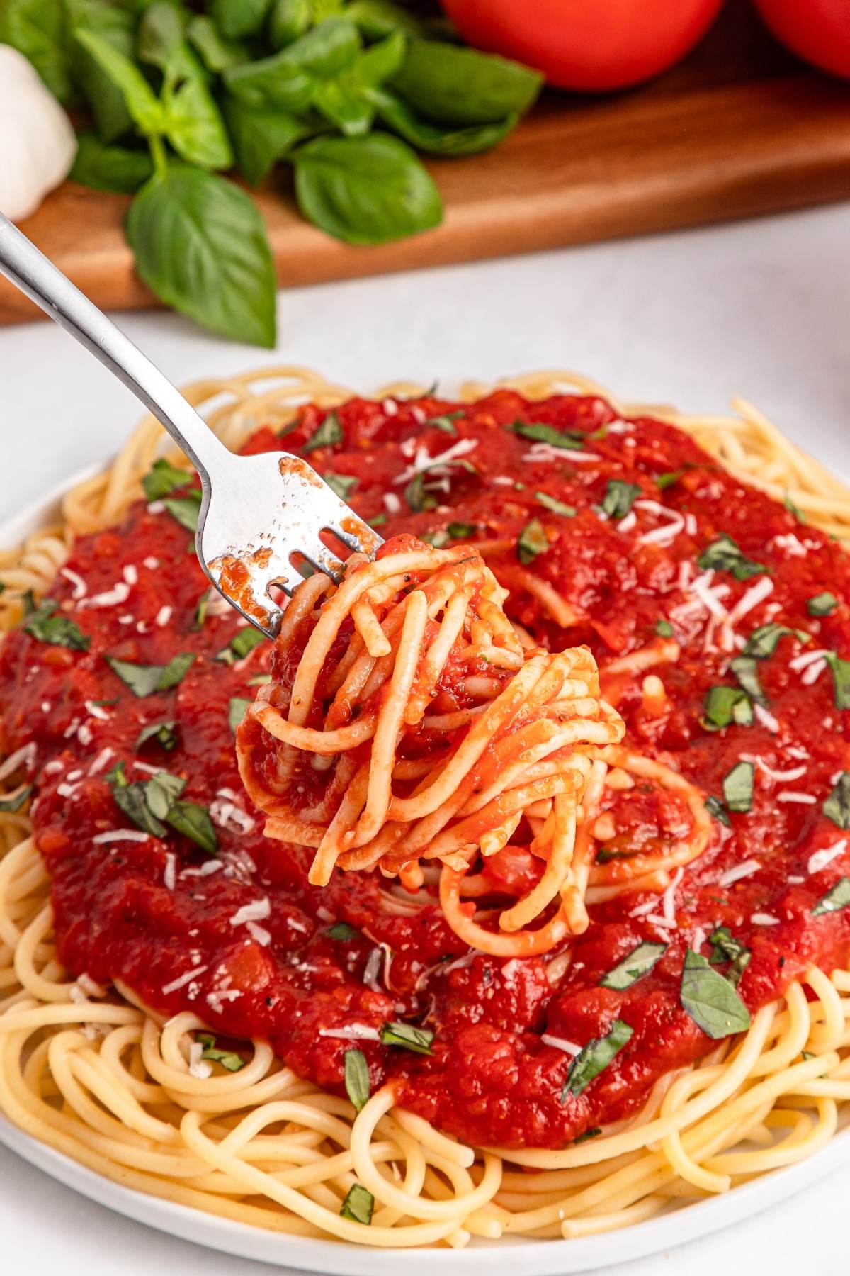 A fork twirls spaghetti with tomato sauce and basil over a plate of pasta, garnished with grated cheese.