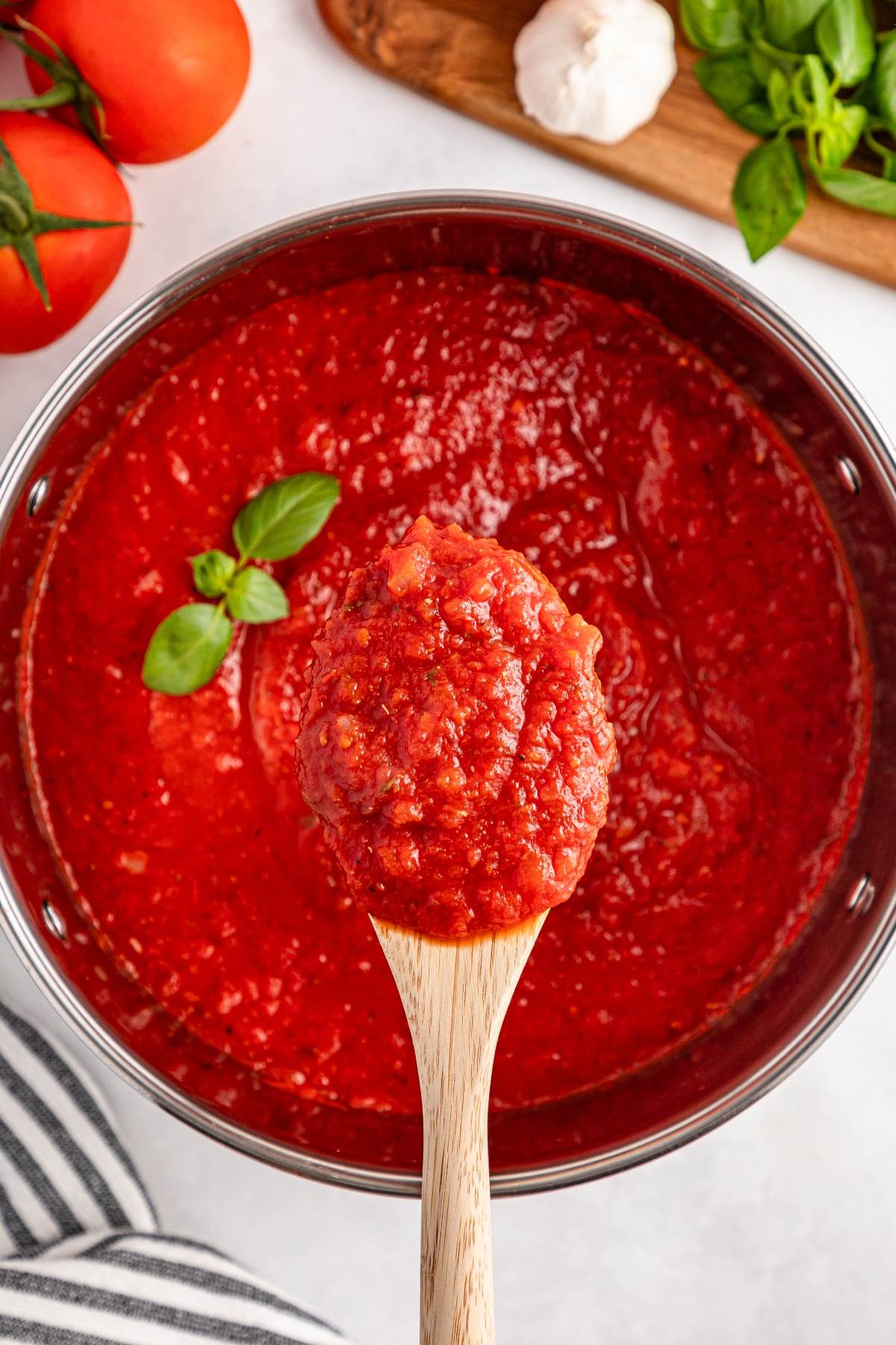 A wooden spoon holding chunky tomato sauce over a pot, garnished with fresh basil.