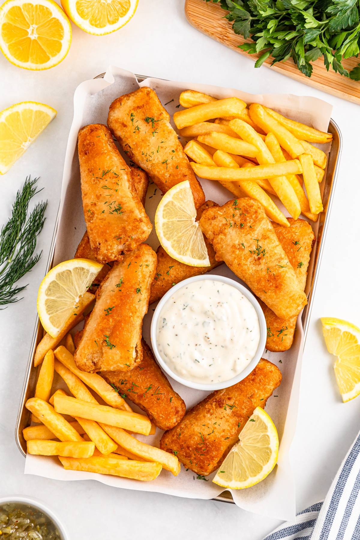 Golden fried fish and crispy fries on a tray with lemon slices and a bowl of tartar sauce.