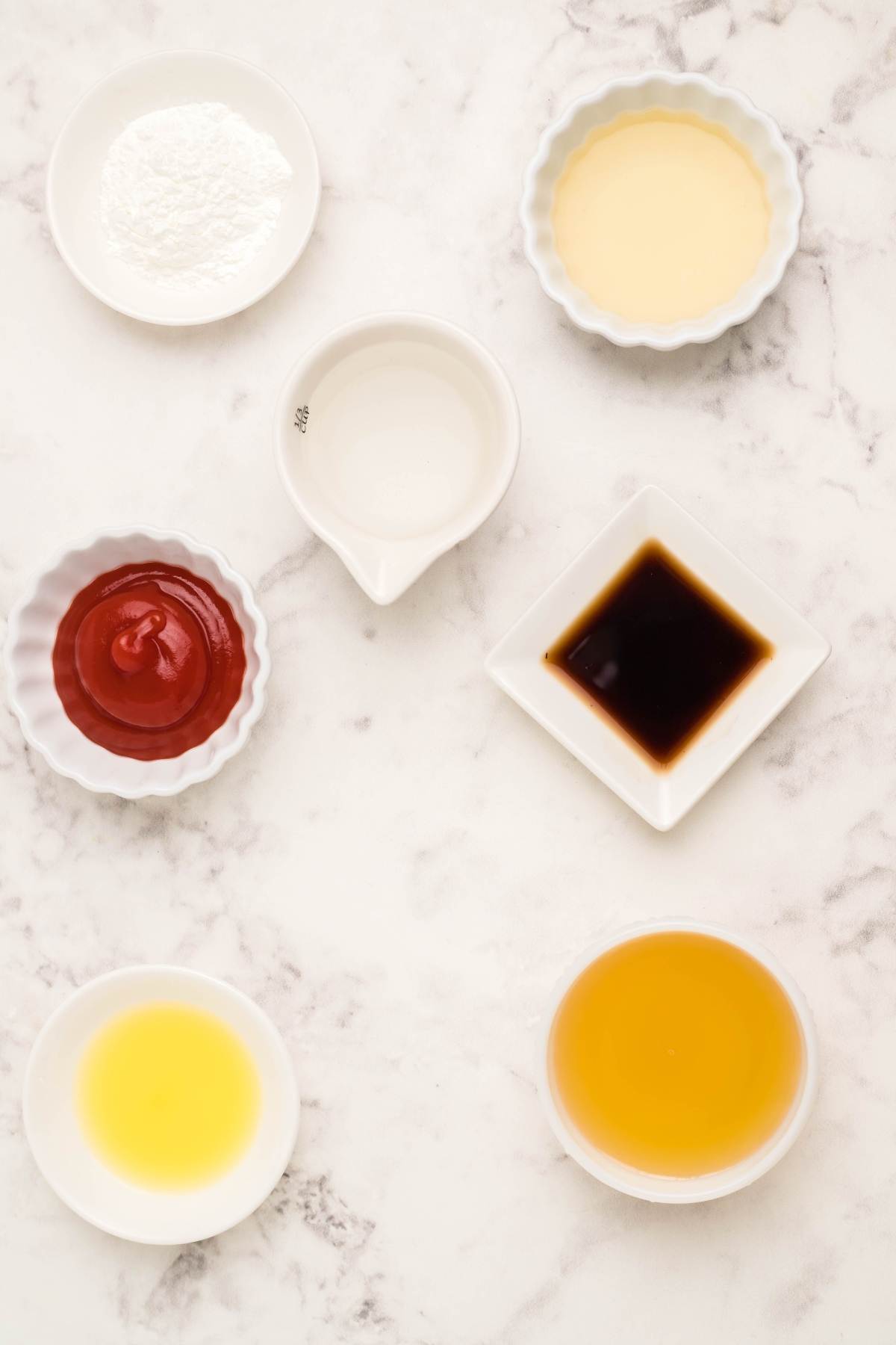 Six small bowls with various sauces and liquids, including a homemade sauce recipe for egg roll sauce and sugar free sweet and sour sauce, arranged on a white marble surface, seen from above.