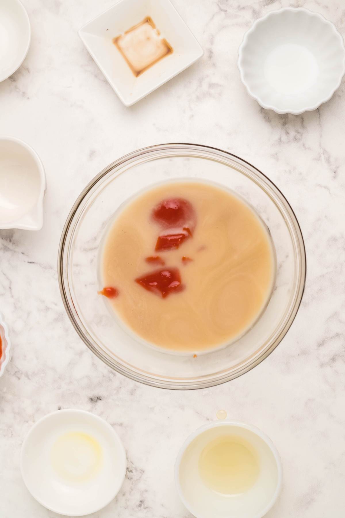 A glass bowl with egg roll sauce and ketchup, surrounded by small empty bowls on a marble surface.