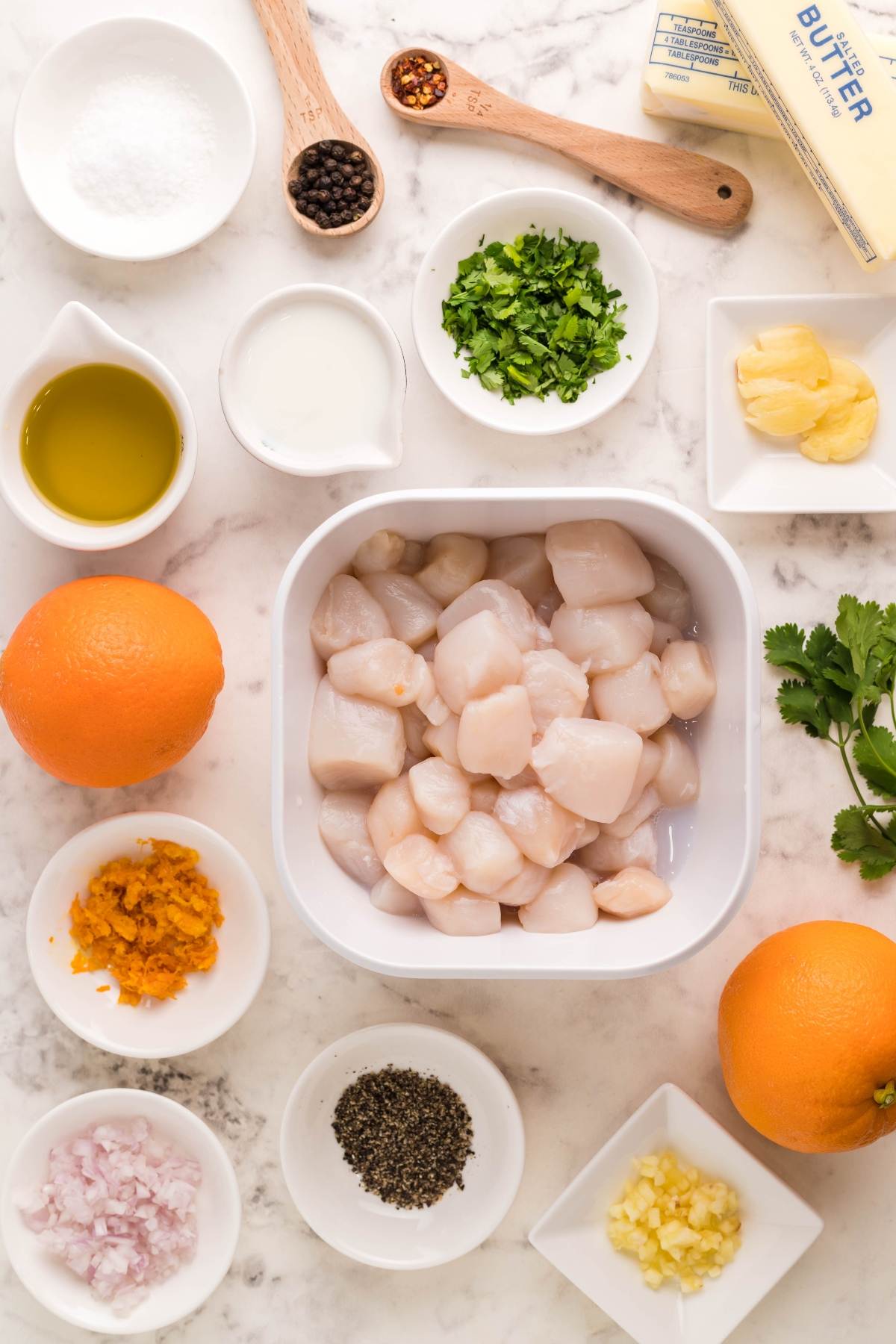 Overhead view of raw scallops in a bowl surrounded by oranges, herbs, spices, butter, oil, and minced ingredients—perfect for making Seafood kabobs on the grill or drizzling with a Citrus Garlic Smoked Butter Sauce.