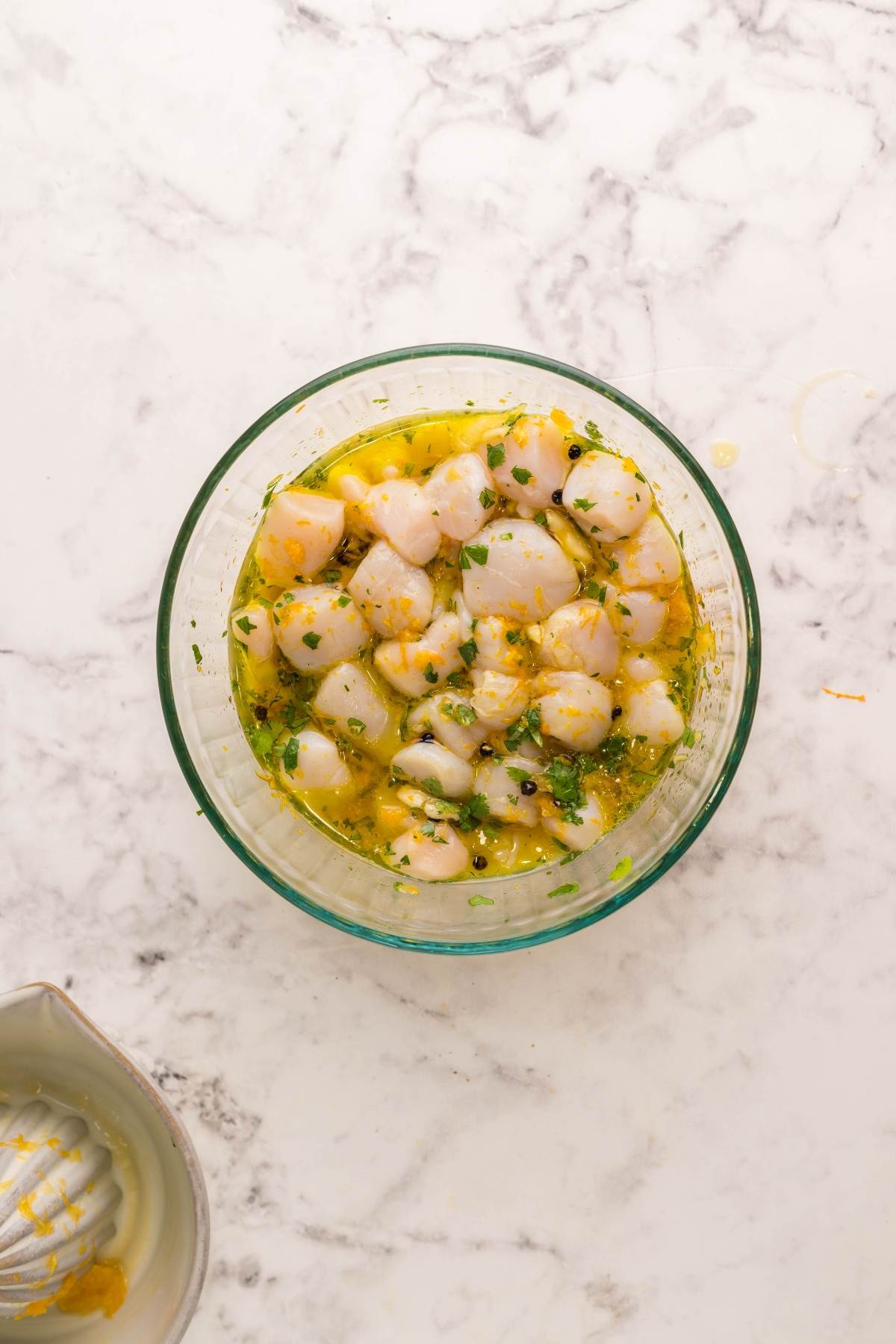 Glass bowl with diced fish marinating in citrus juice and herbs on a marble countertop, perfect to serve alongside BBQ scallop skewers for a fresh seafood feast.