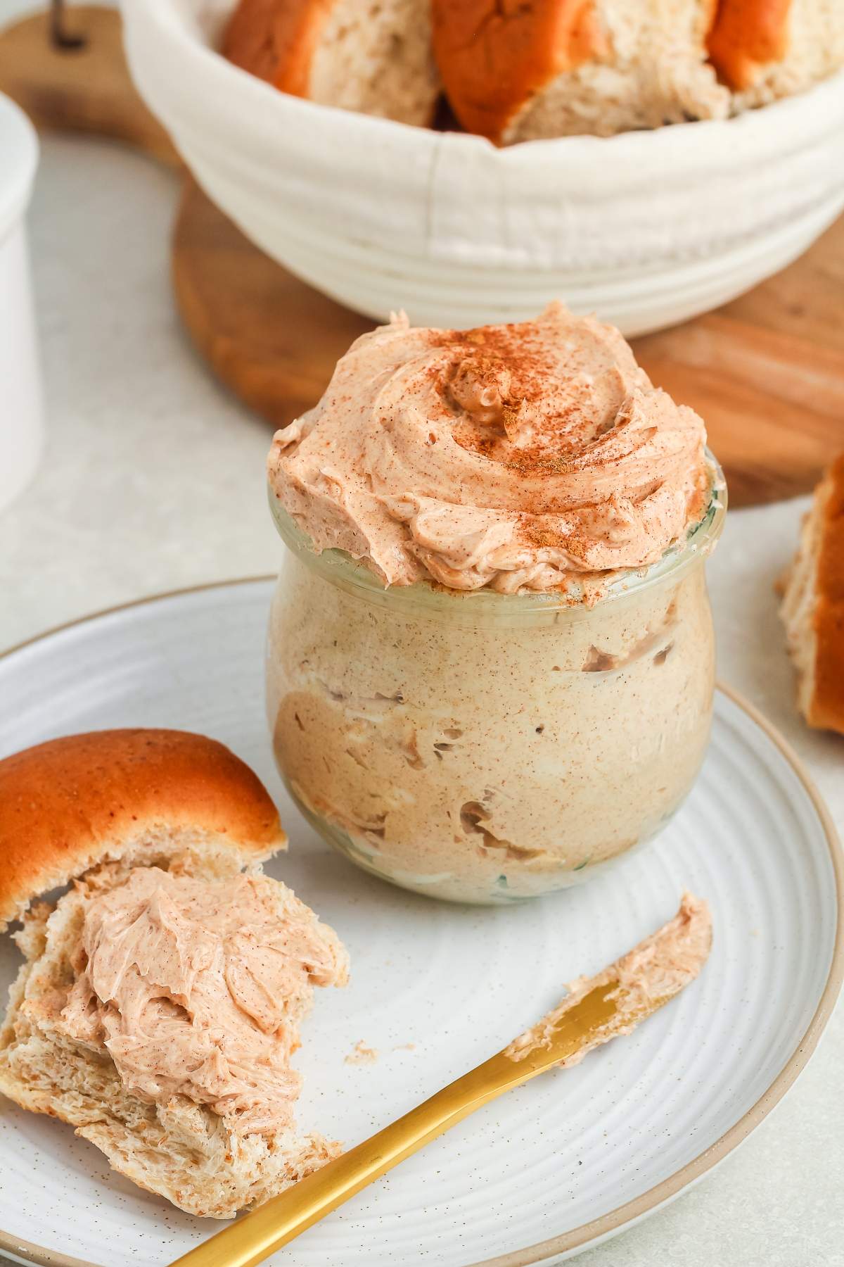 A jar of whipped cinnamon butter with a swirl on top, next to a plate with bread and a gold knife.