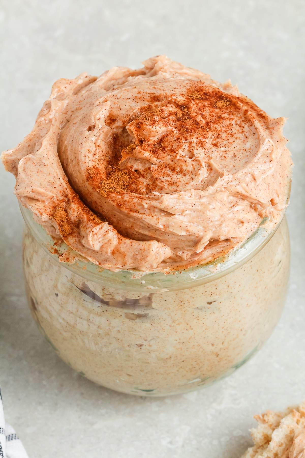 A small glass jar filled with whipped cinnamon butter, sprinkled with cinnamon on top.