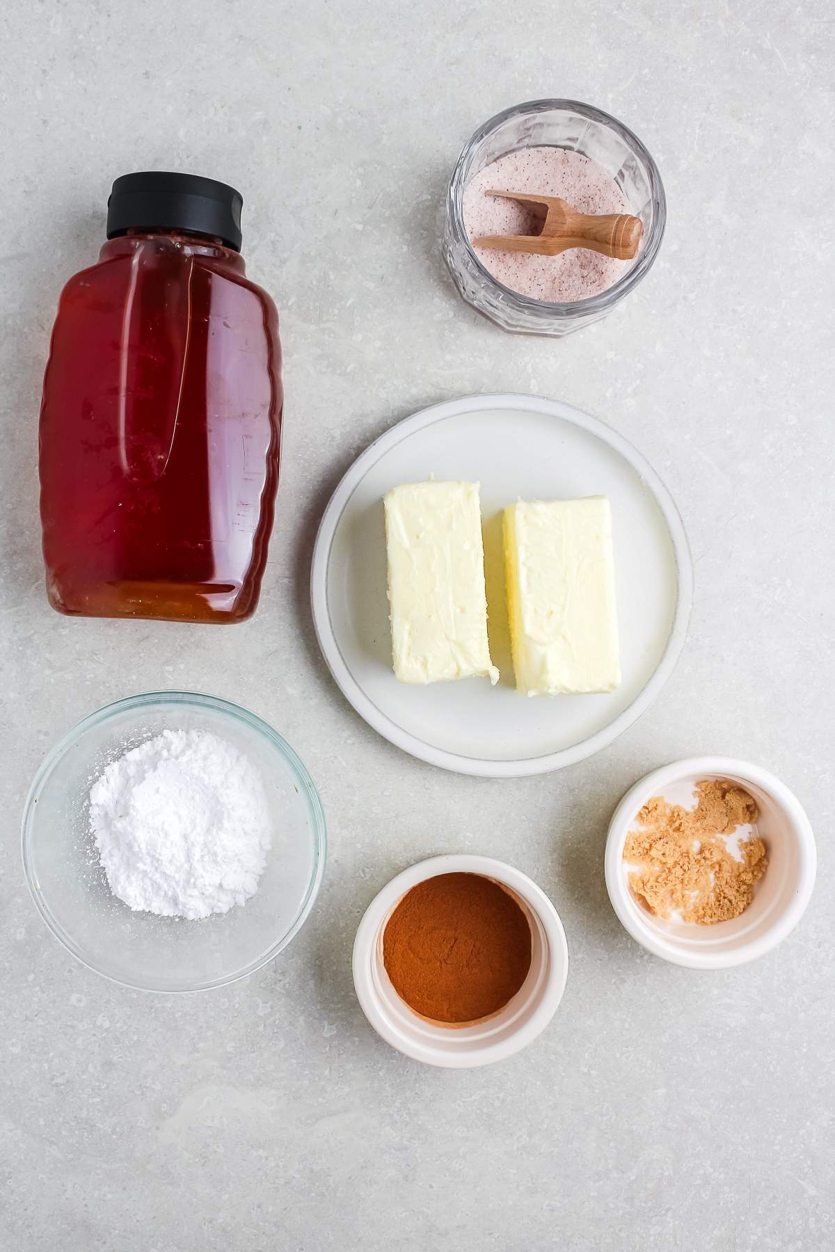 Honey, two butter sticks, cinnamon, powdered sugar, brown sugar, and pink salt on a light countertop.