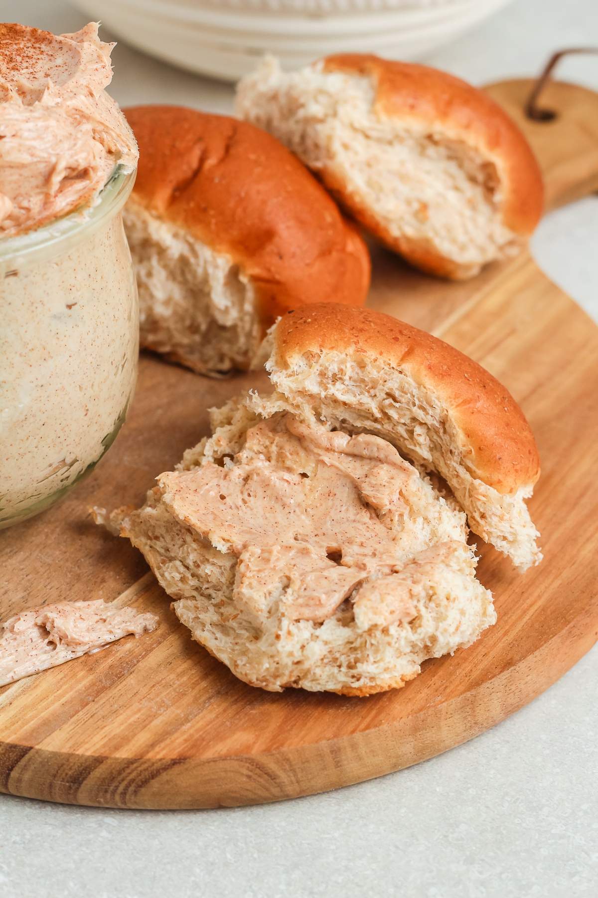 A wooden board with rolls spread with cinnamon butter, next to a jar of the spread.