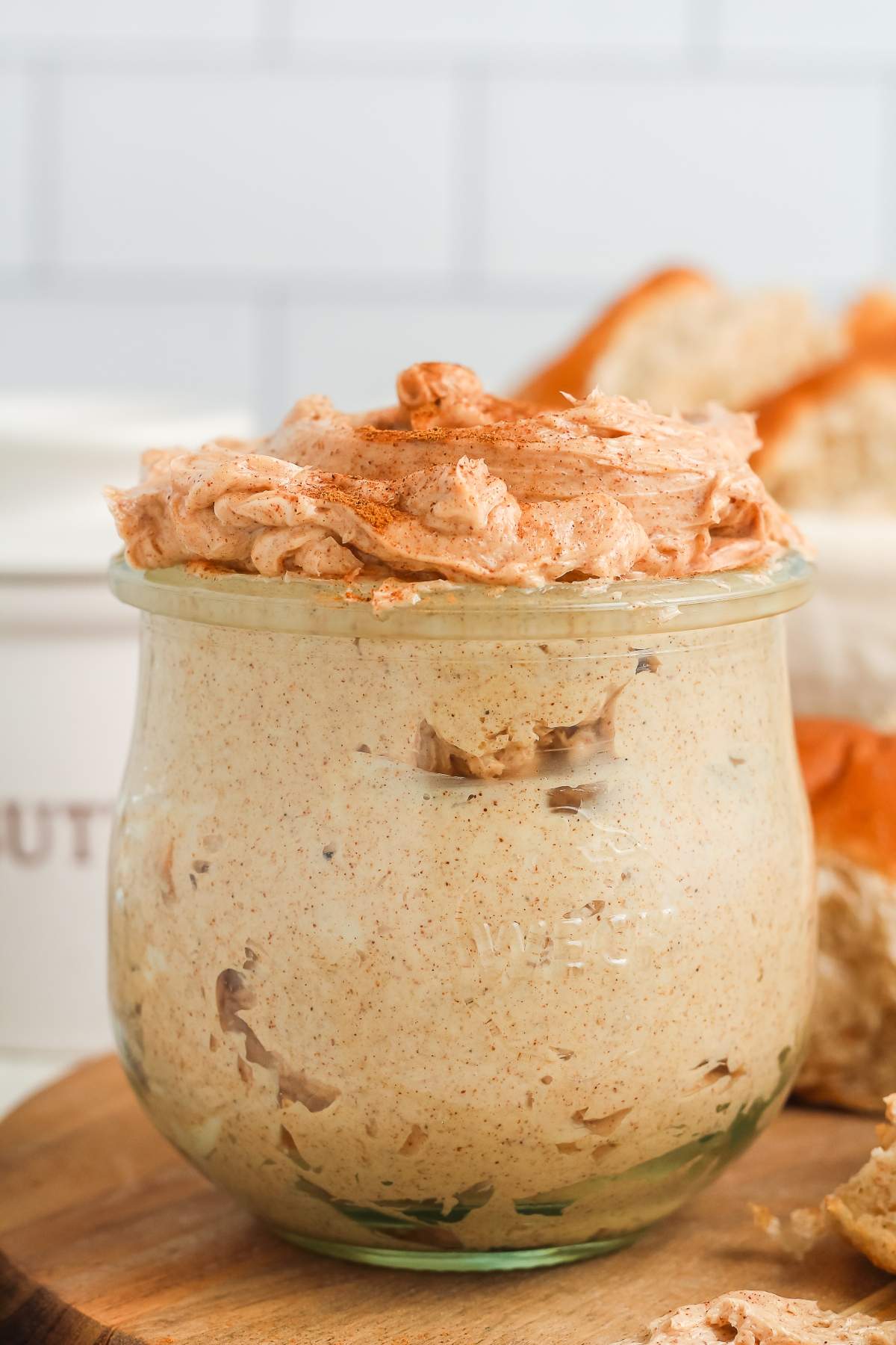 A glass jar filled with creamy, cinnamon butter, with bread in the background.