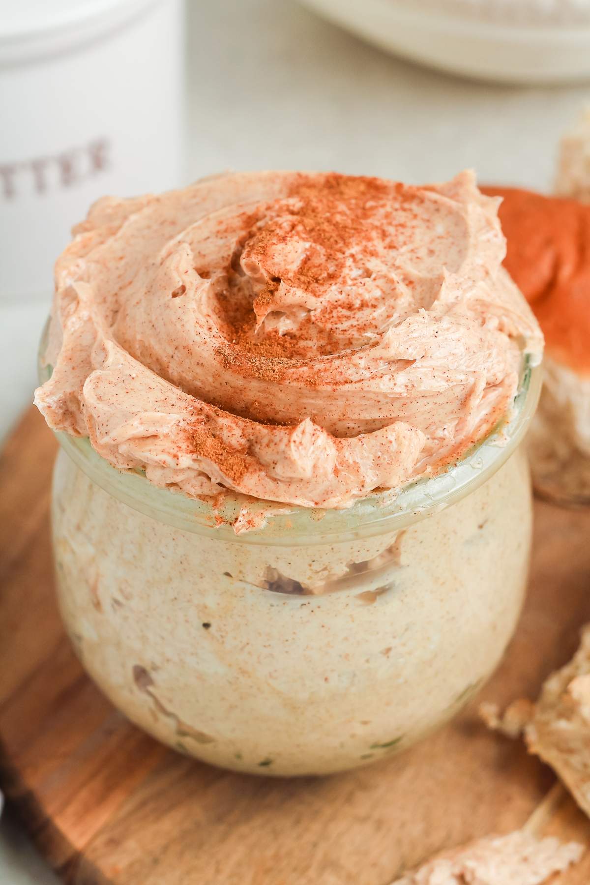 A jar of whipped cinnamon butter topped with a sprinkle of cinnamon, on a wooden board.