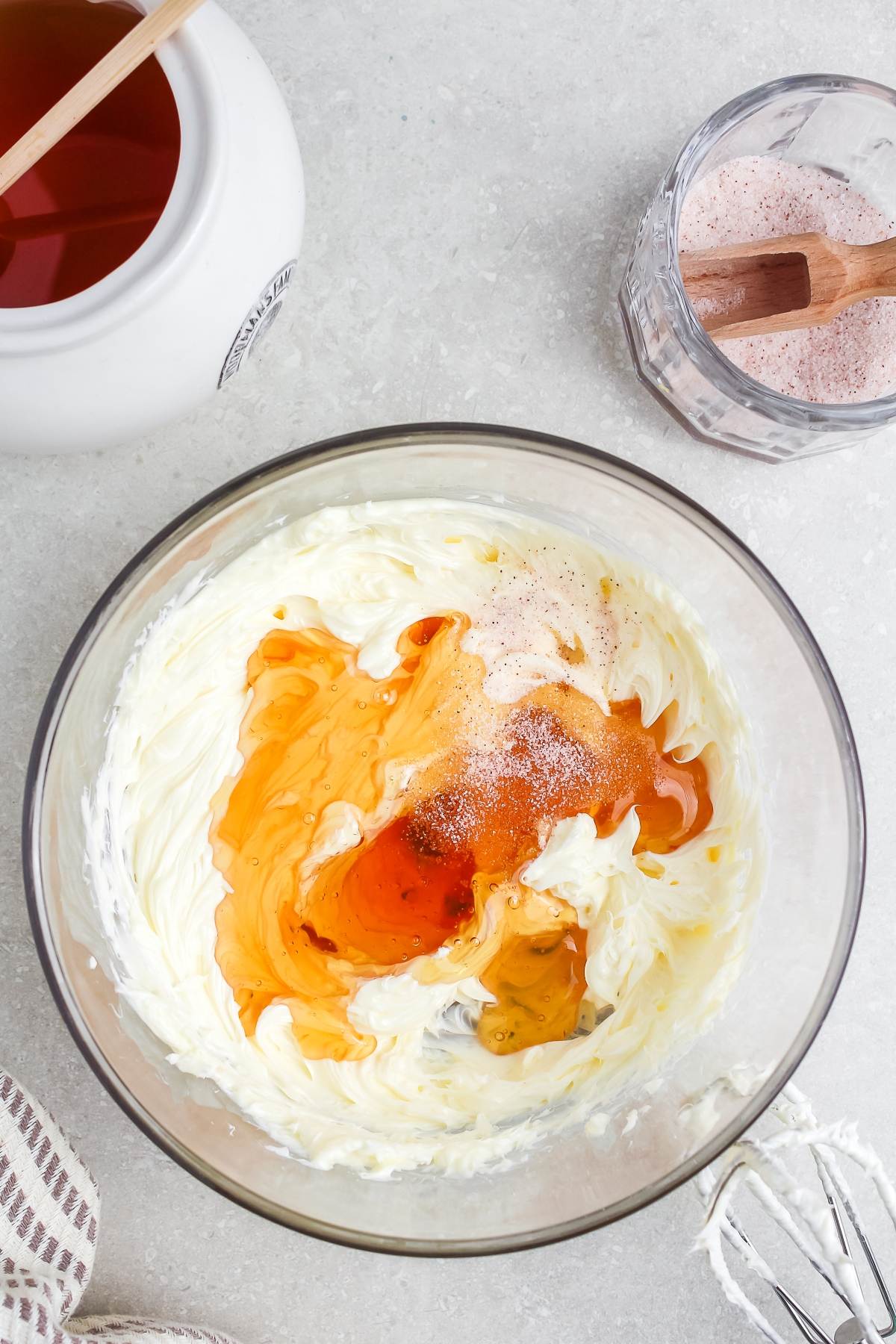 Cream cheese mixture in a bowl with honey and vanilla, next to a jar of honey and a glass of brown sugar.