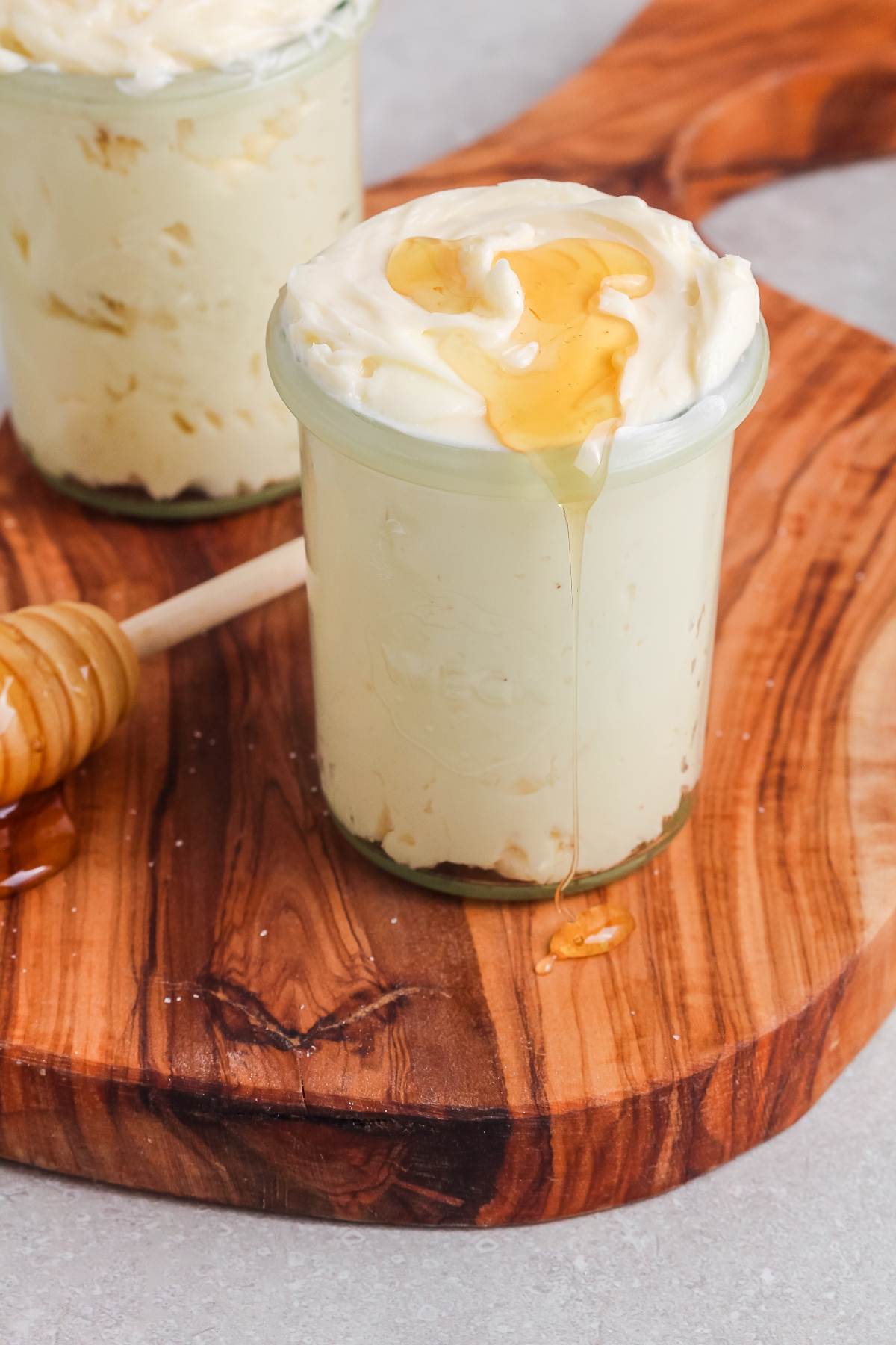 Glass jar of creamy butter spread with honey drizzle on top, sitting on a wooden board.