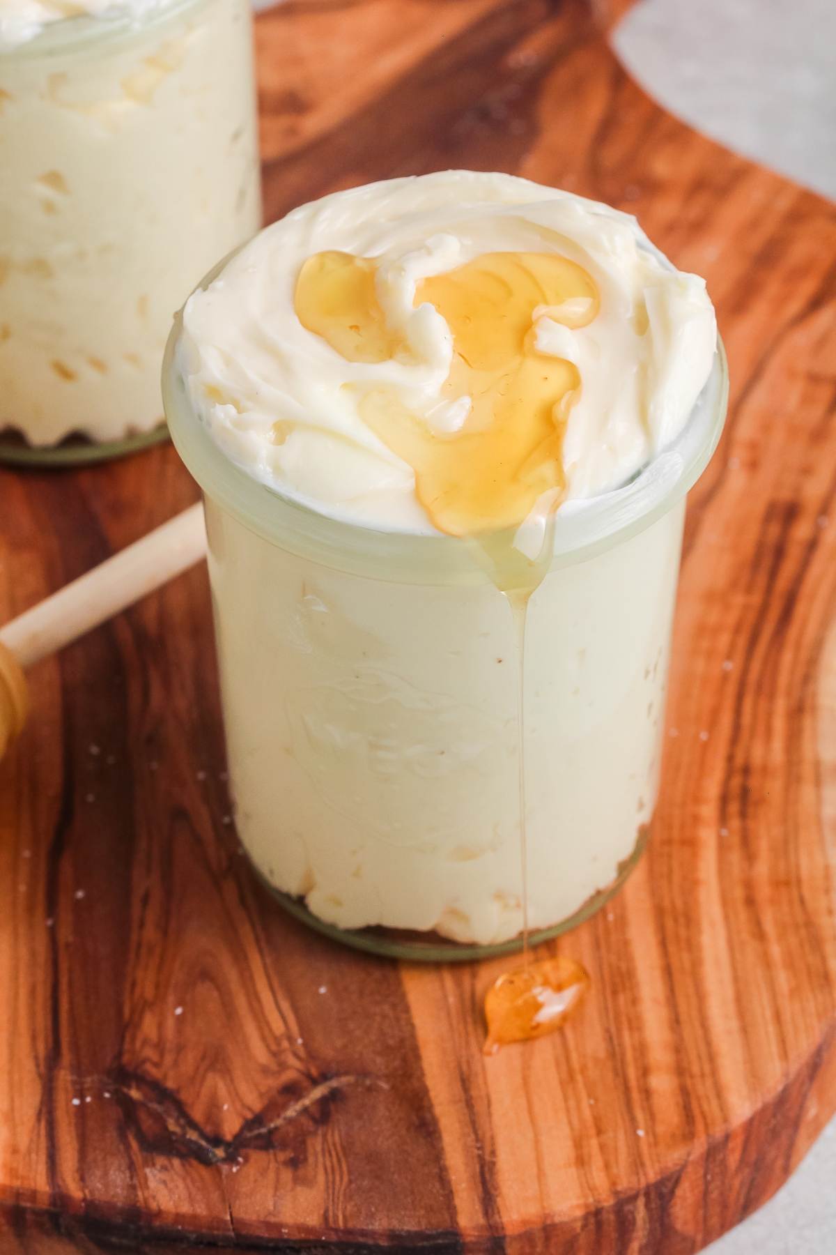 A glass jar of creamy whipped butter topped with honey, sitting on a wooden board.