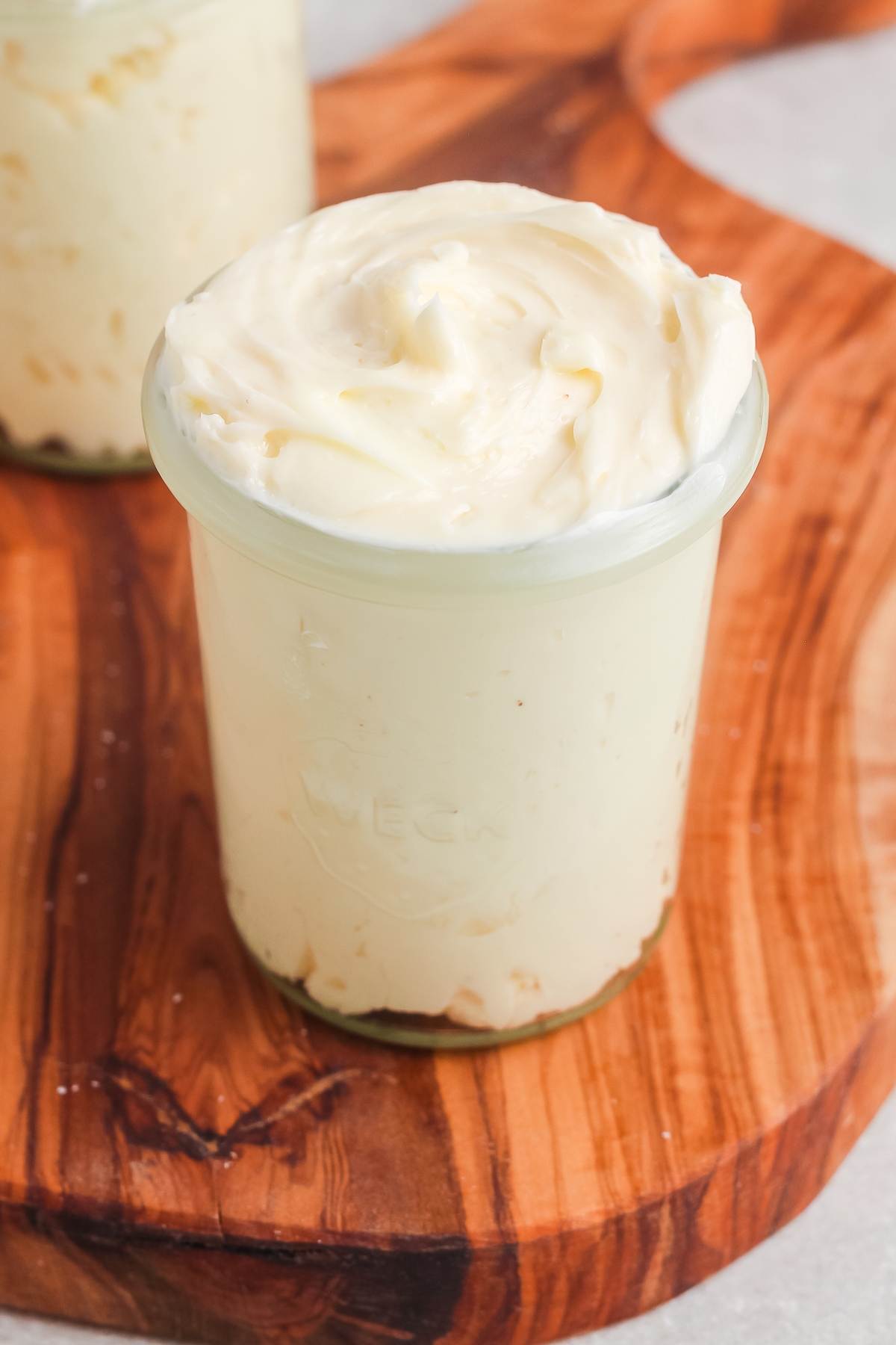 A small glass jar filled with creamy cheesecake on a wooden board.