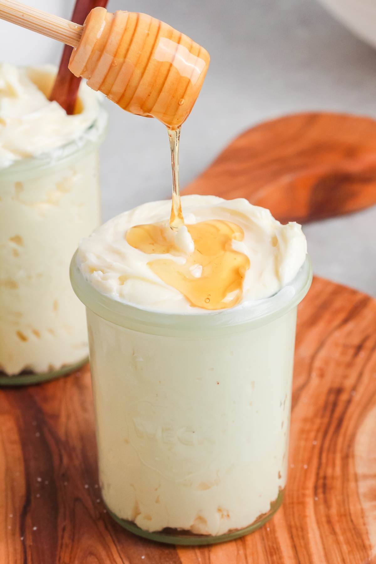 Honey being drizzled over whipped butter in a glass jar on a wooden board.