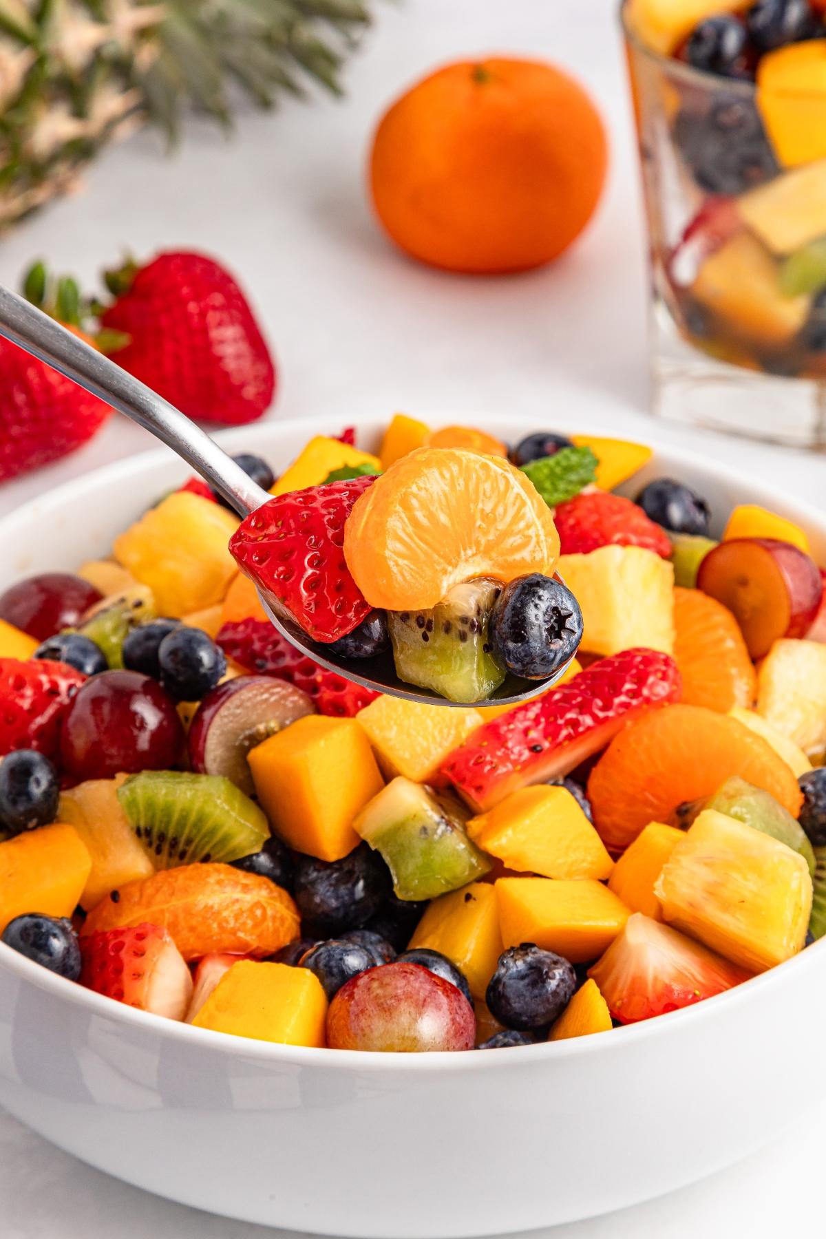 A spoonful of colorful mixed fruit salad with blueberries, grapes, kiwi, strawberries, and oranges.