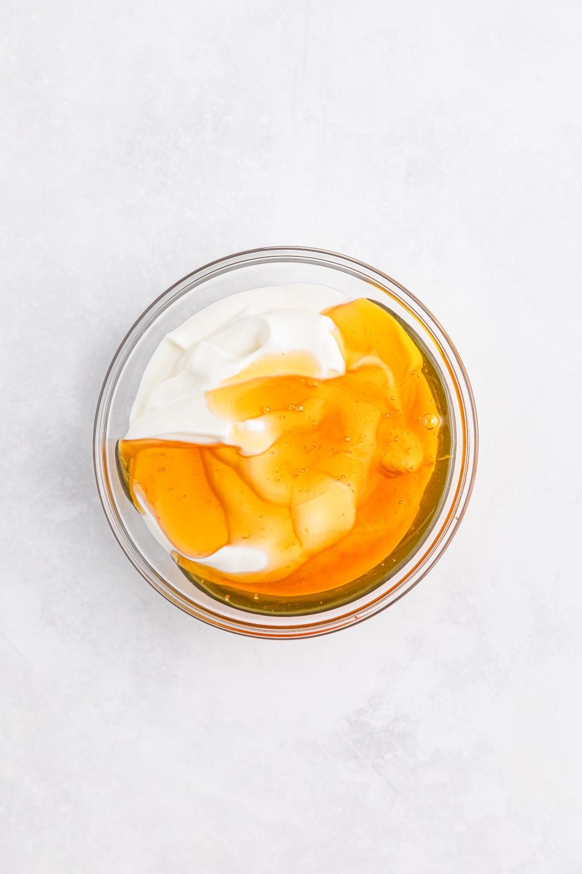 A glass bowl of yogurt topped with honey, photographed from above on a light background.