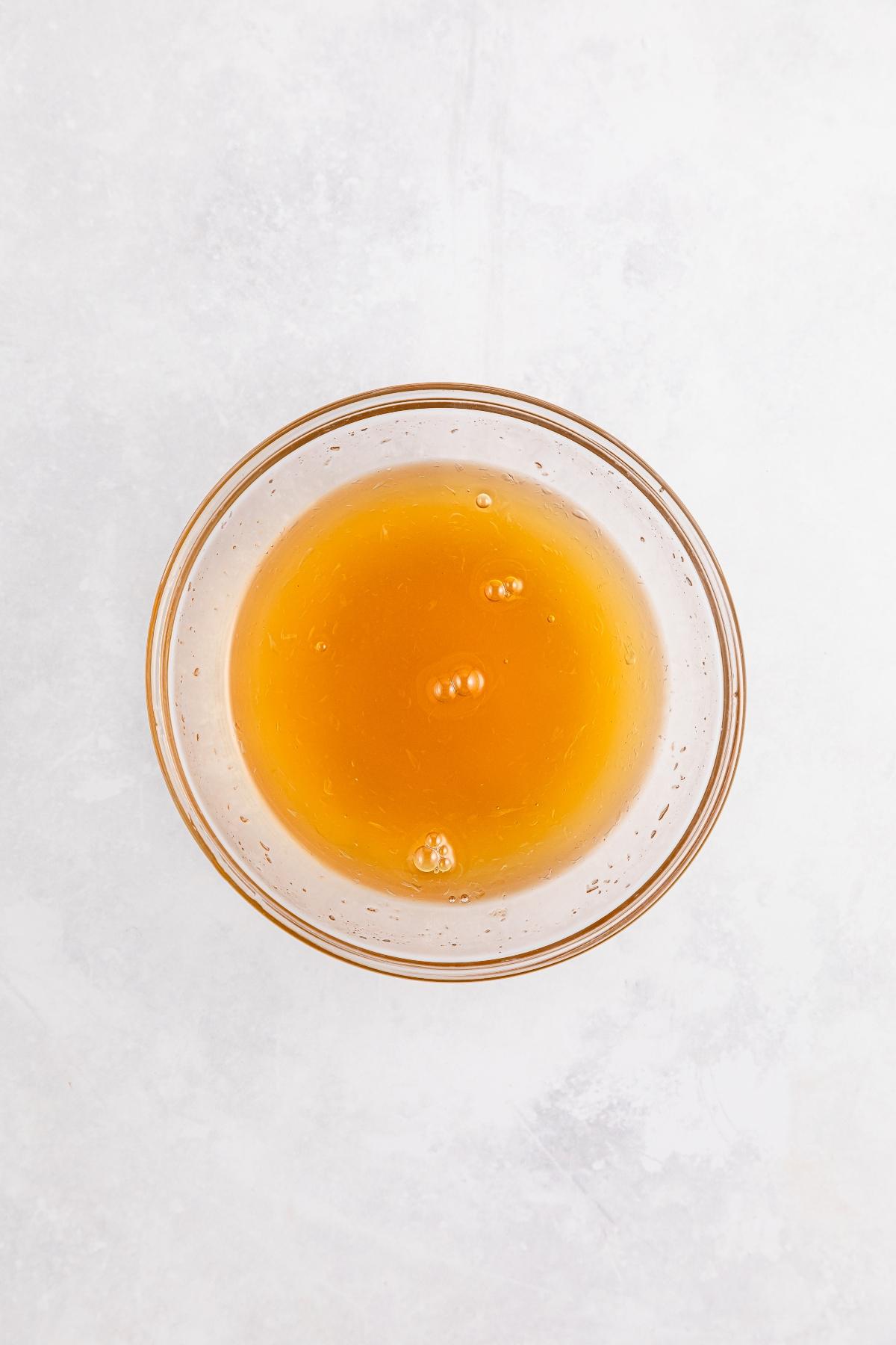 A glass bowl filled with golden honey on a light, textured surface.